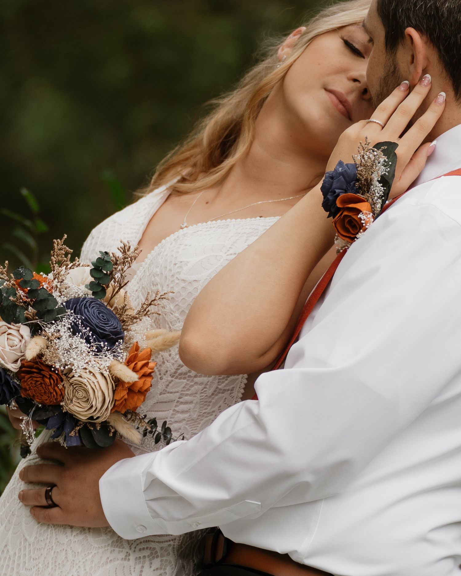 Wedding couple embracing while holding autumn-colored floral bouquet against natural backdrop.