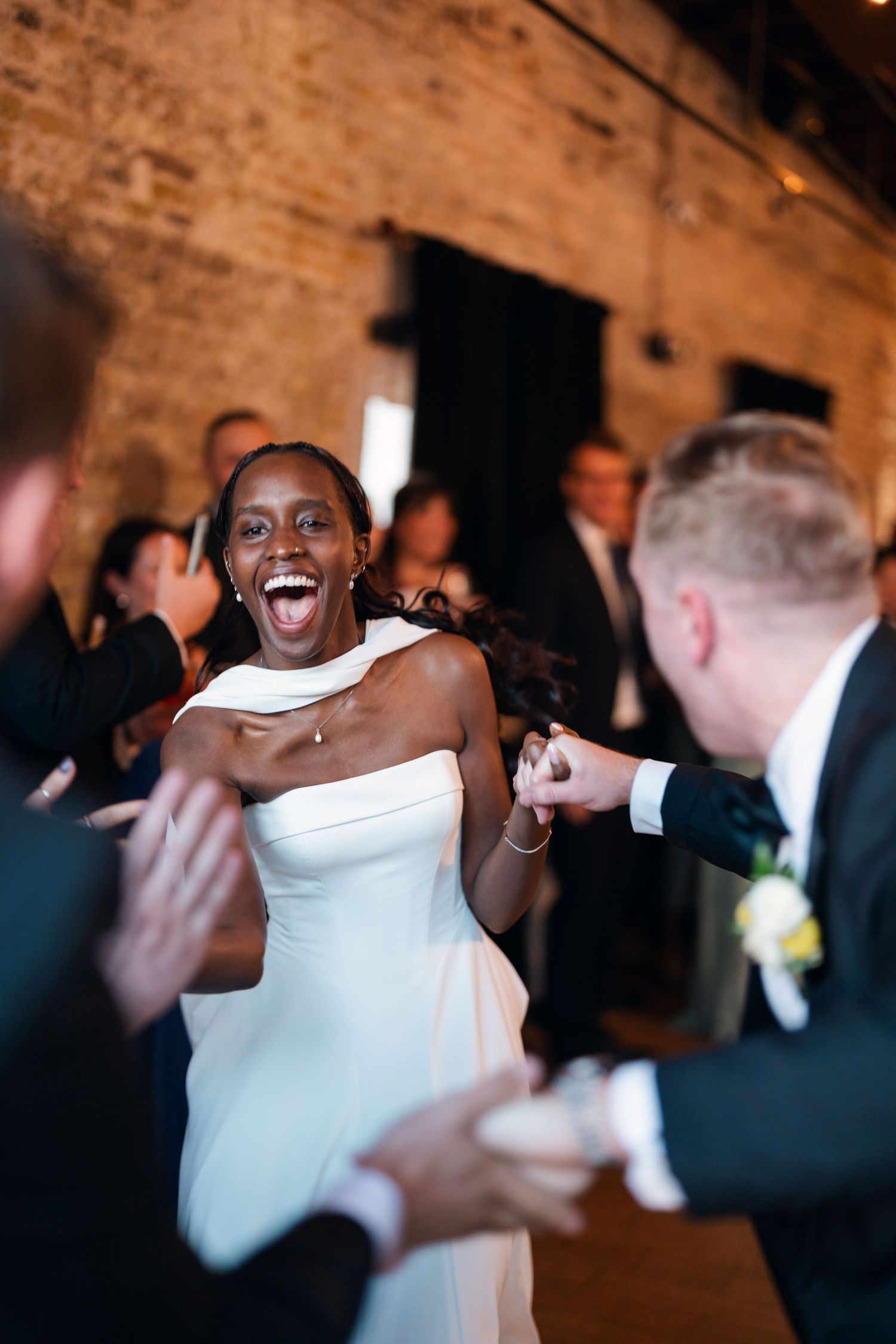 Joyful Black bride laughing while dancing with groom at their wedding reception in a brick venue.