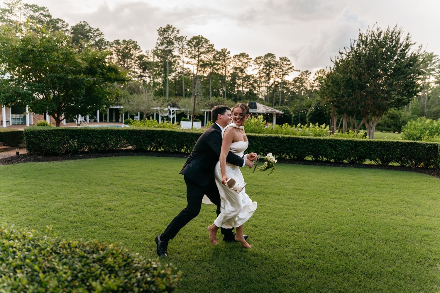 A couple shares a romantic embrace on a lush green lawn during an outdoor photo session at sunset.