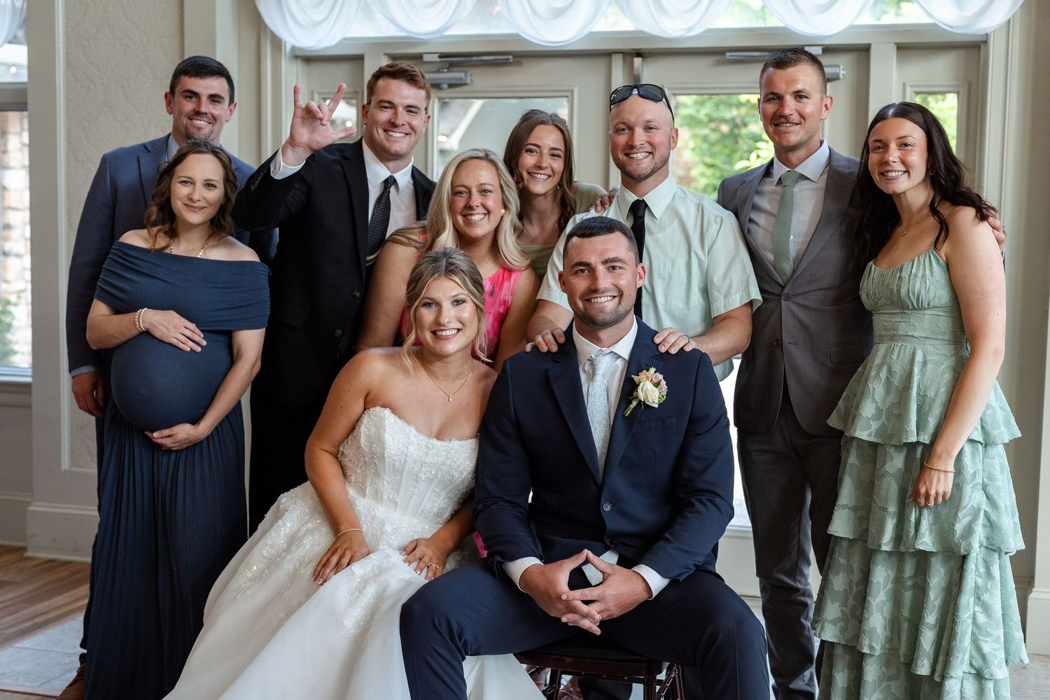 Bride and groom pose with smiling wedding guests indoors for a joyful group portrait photo.