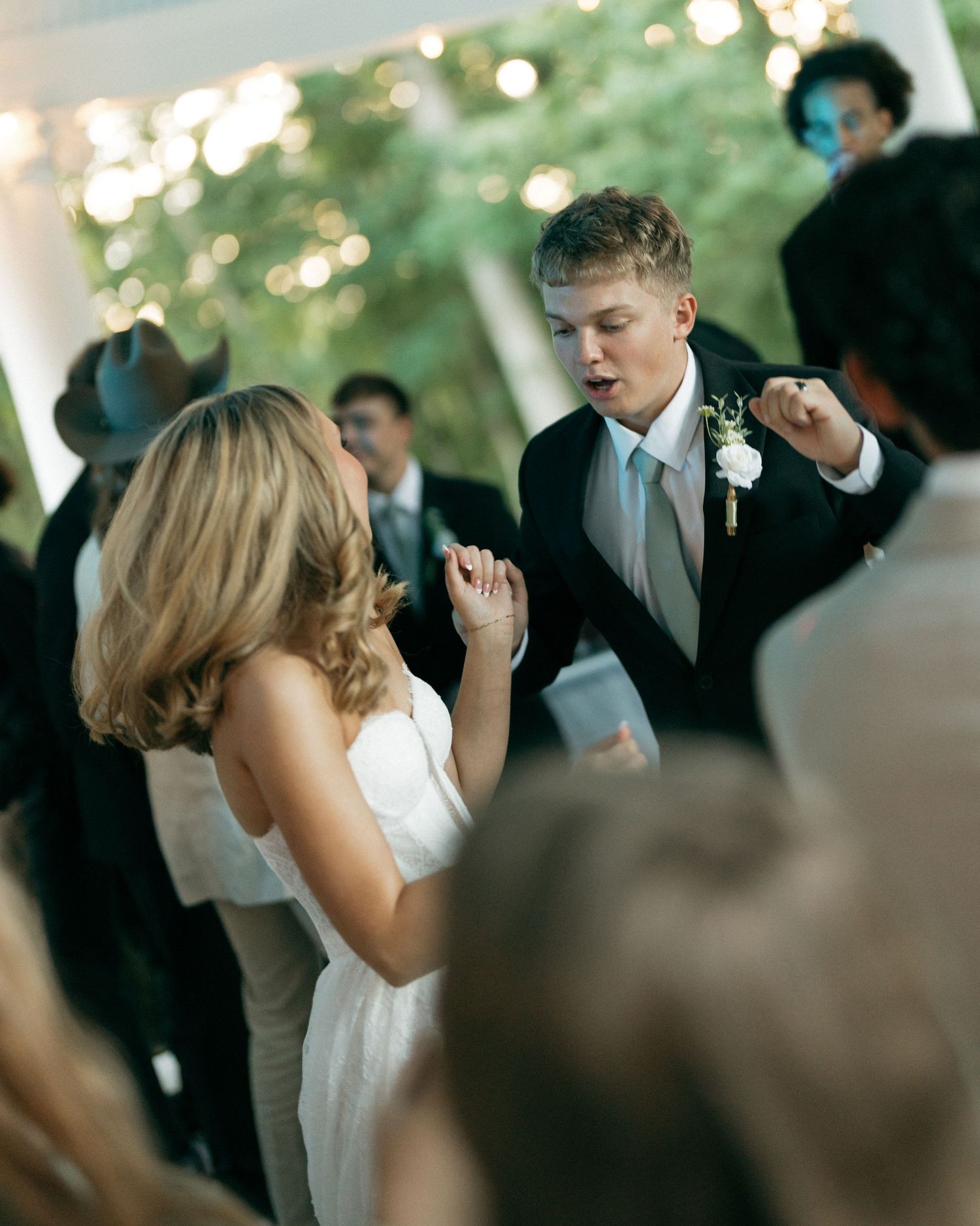 Young groom in black suit with boutonniere dancing energetically with bride in white dress at wedding reception.