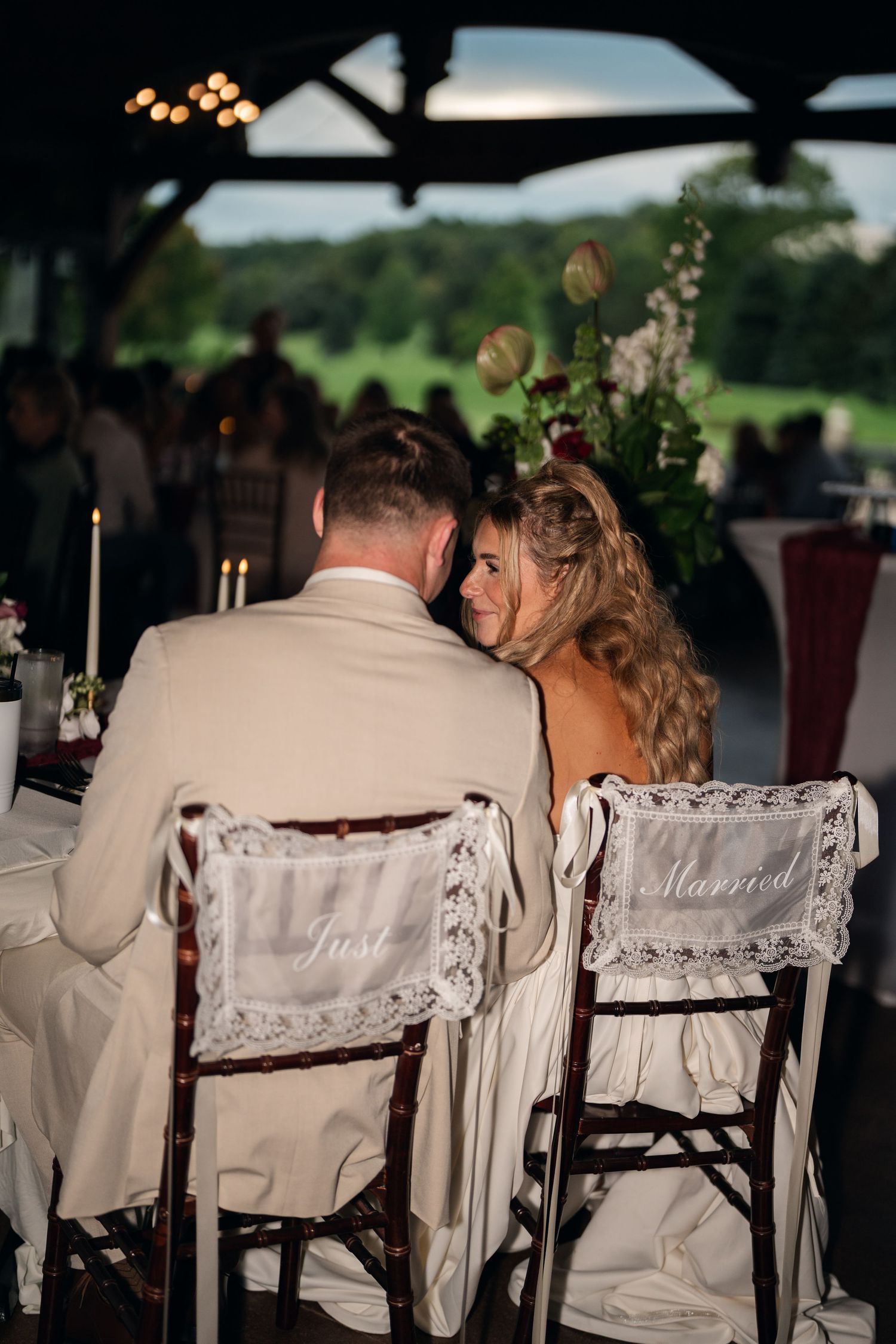 Newlyweds sit in decorated chairs labeled Just Married at their elegant outdoor wedding reception.