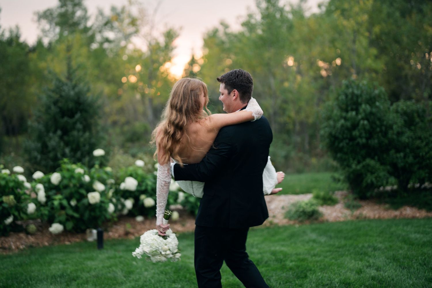 Bride and groom embracing on green lawn at sunset in garden wedding.