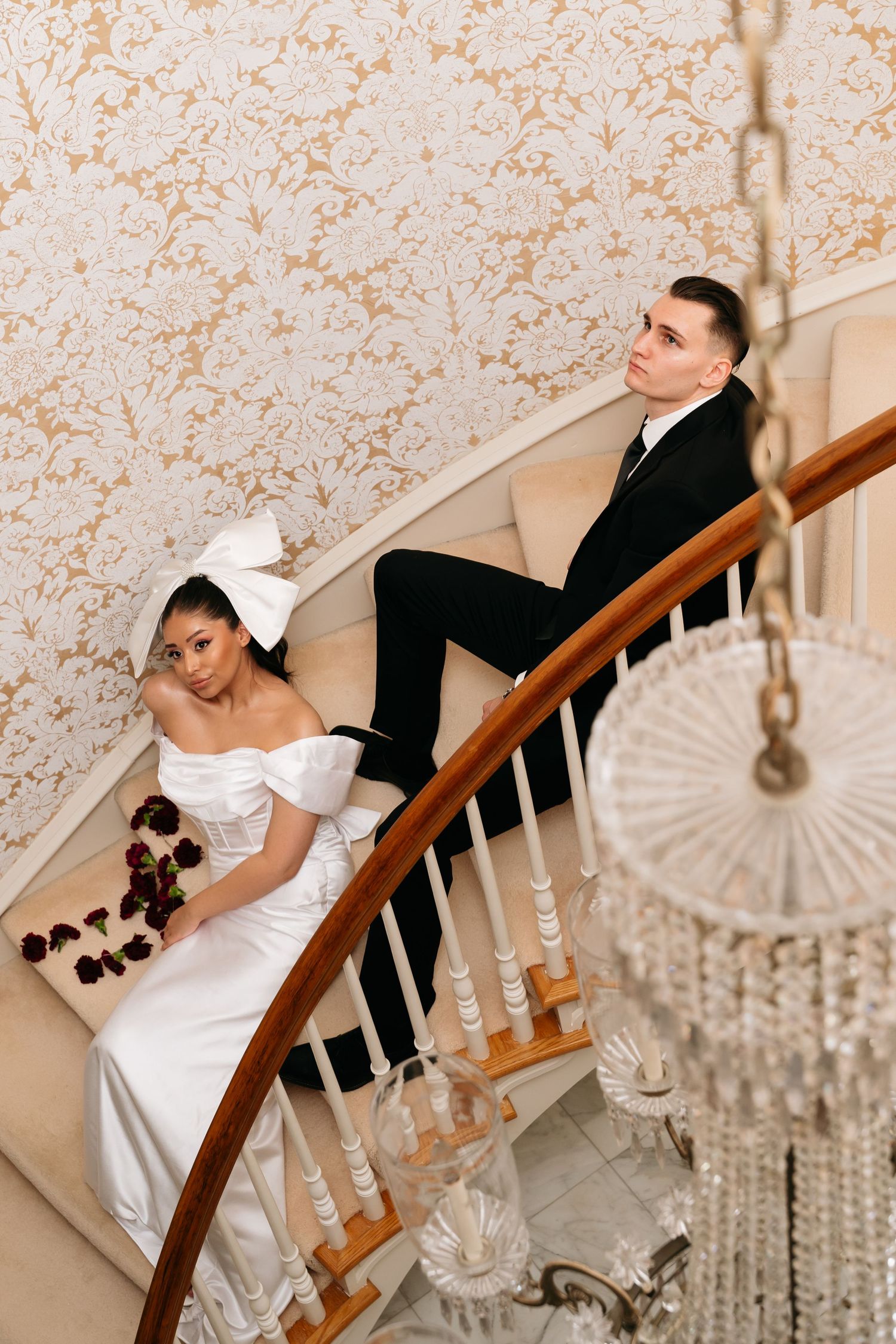 Elegant bride and groom posing on a curved staircase, bride in white gown with bow, groom in black suit.