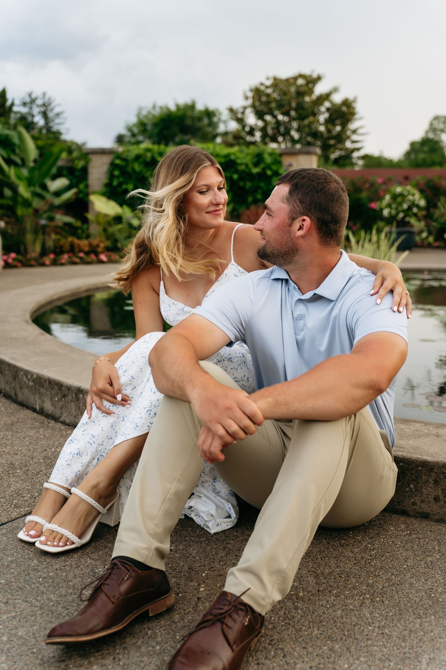 A couple sits casually together on concrete steps wearing coordinating white and khaki outfits in an outdoor setting.