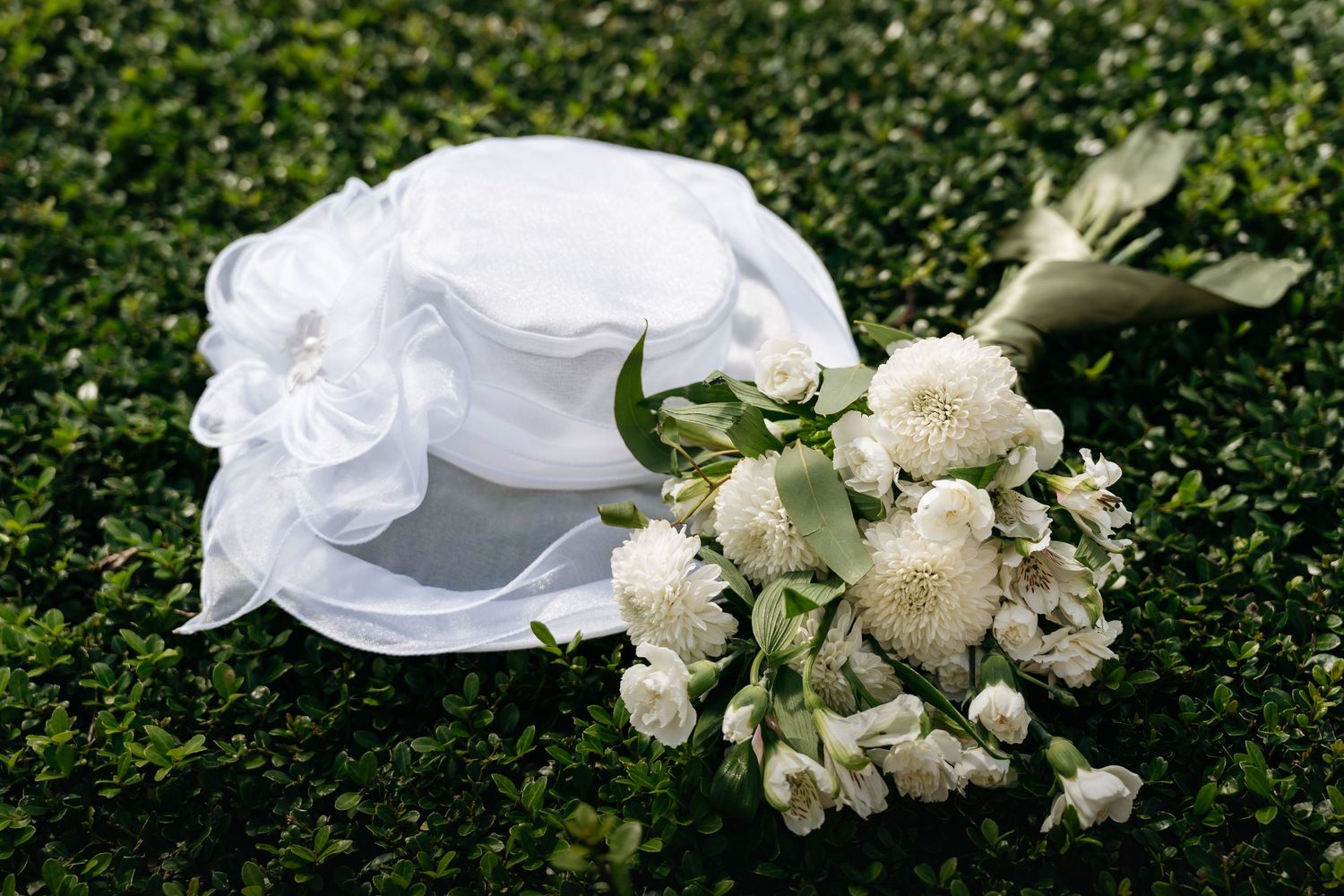 A white veil blowing in the wind next to delicate white roses against a green hedge background.