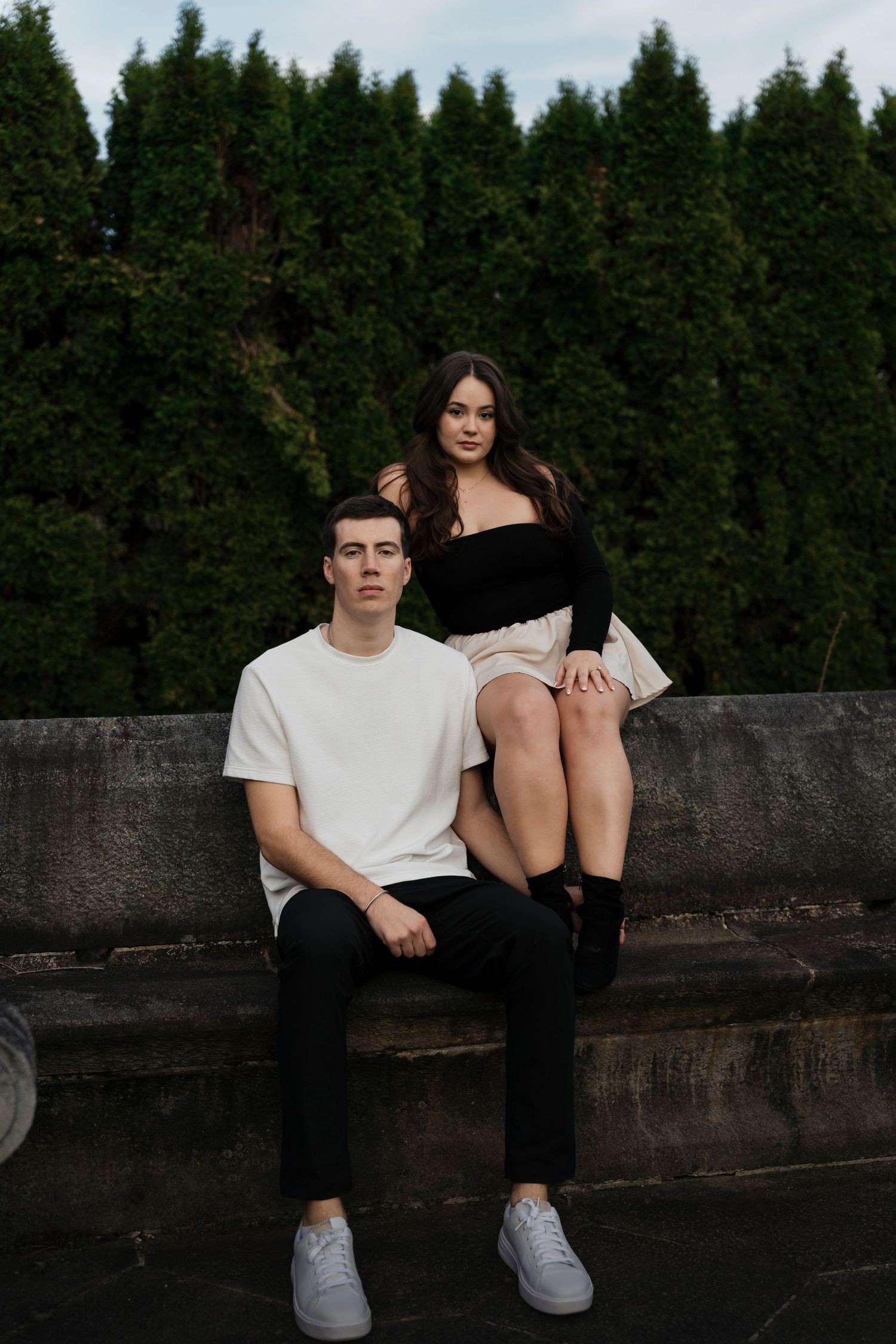 Editorial style engagement photo of couple in black attire with sunlight filtering through garden trees