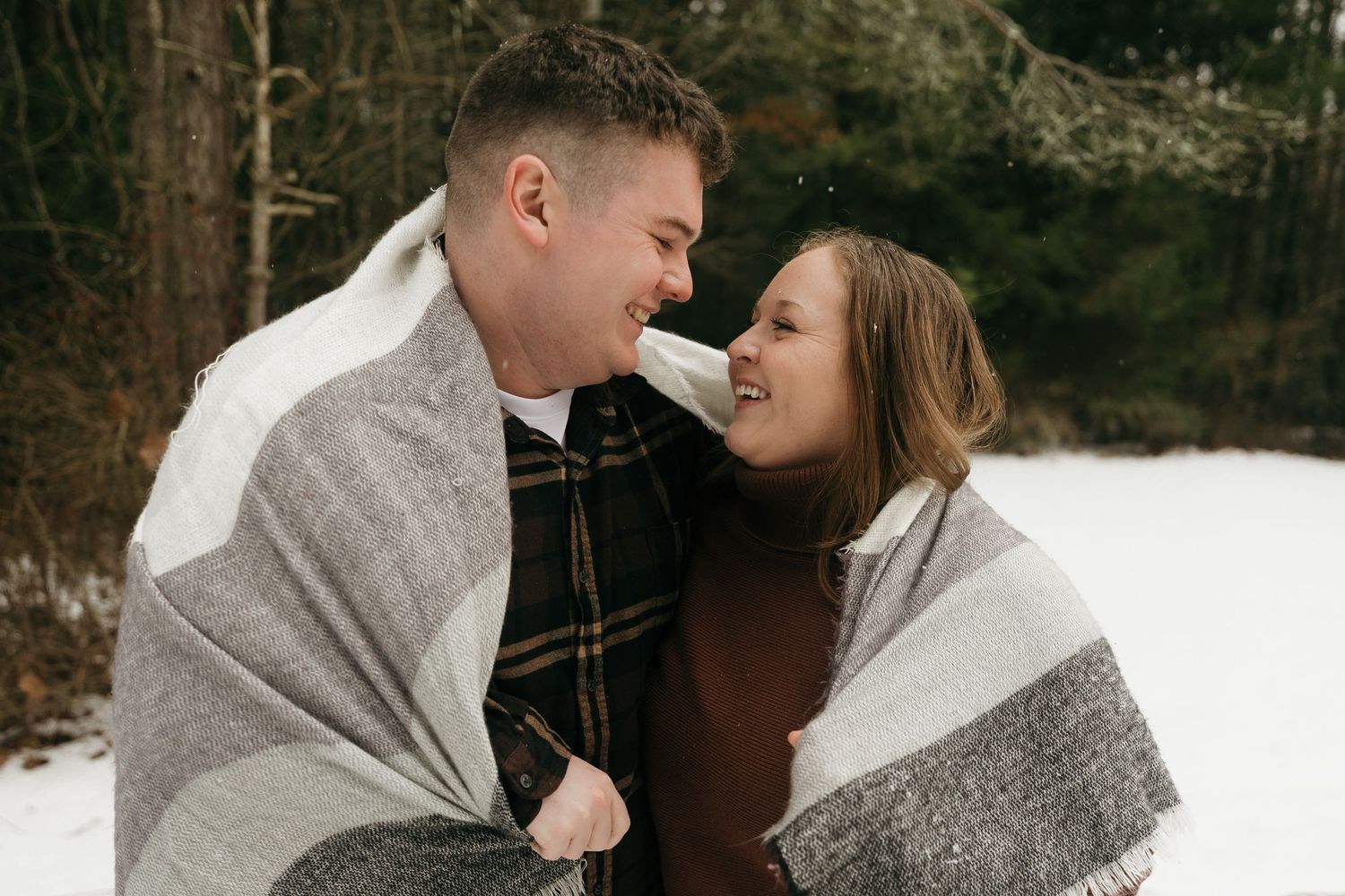 A couple wrapped in a blanket sharing a tender moment in the snow.