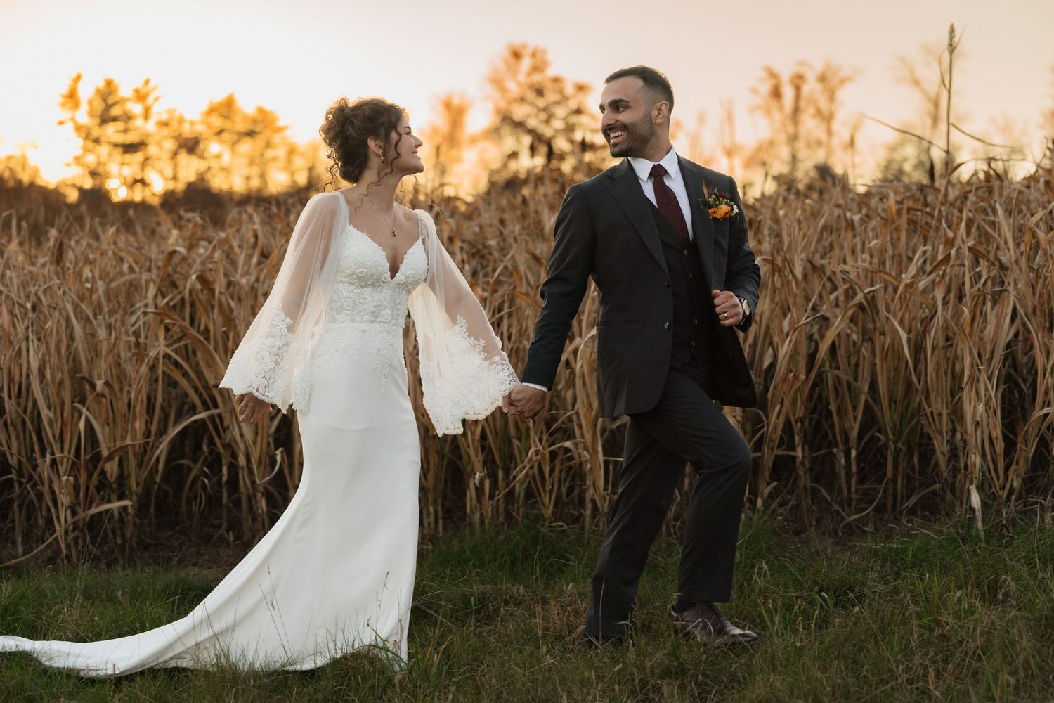 Wedding couple poses in golden autumn field at sunset with warm sunlight shining through tall grass.