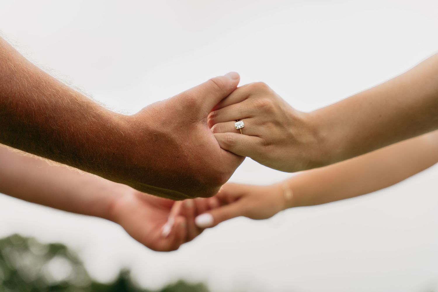 Two hands reaching out to hold each other against a blurred light background.