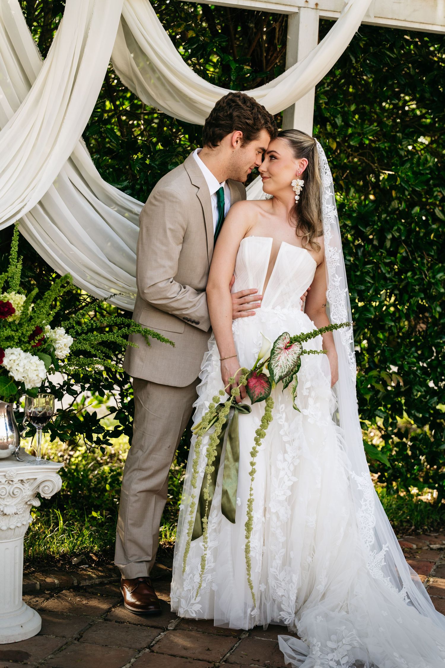 Romantic wedding couple shares intimate moments under white draped gazebo in garden setting.