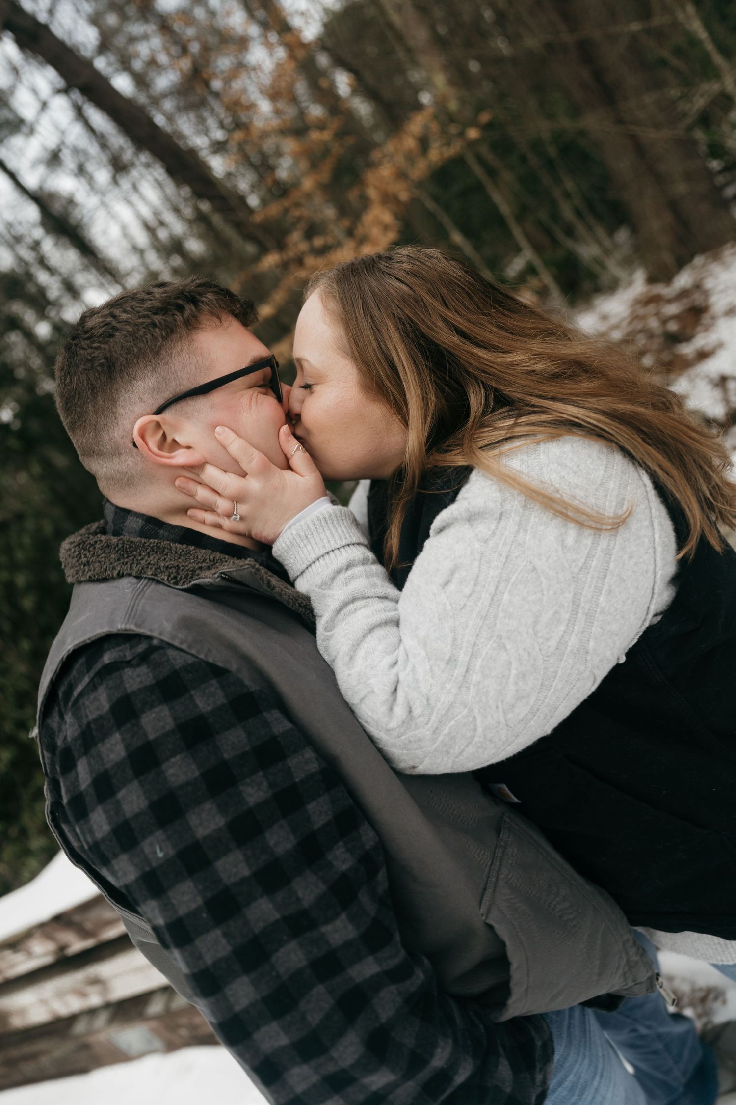 An intimate winter engagement photo captures a couple sharing a tender kiss in the snow.