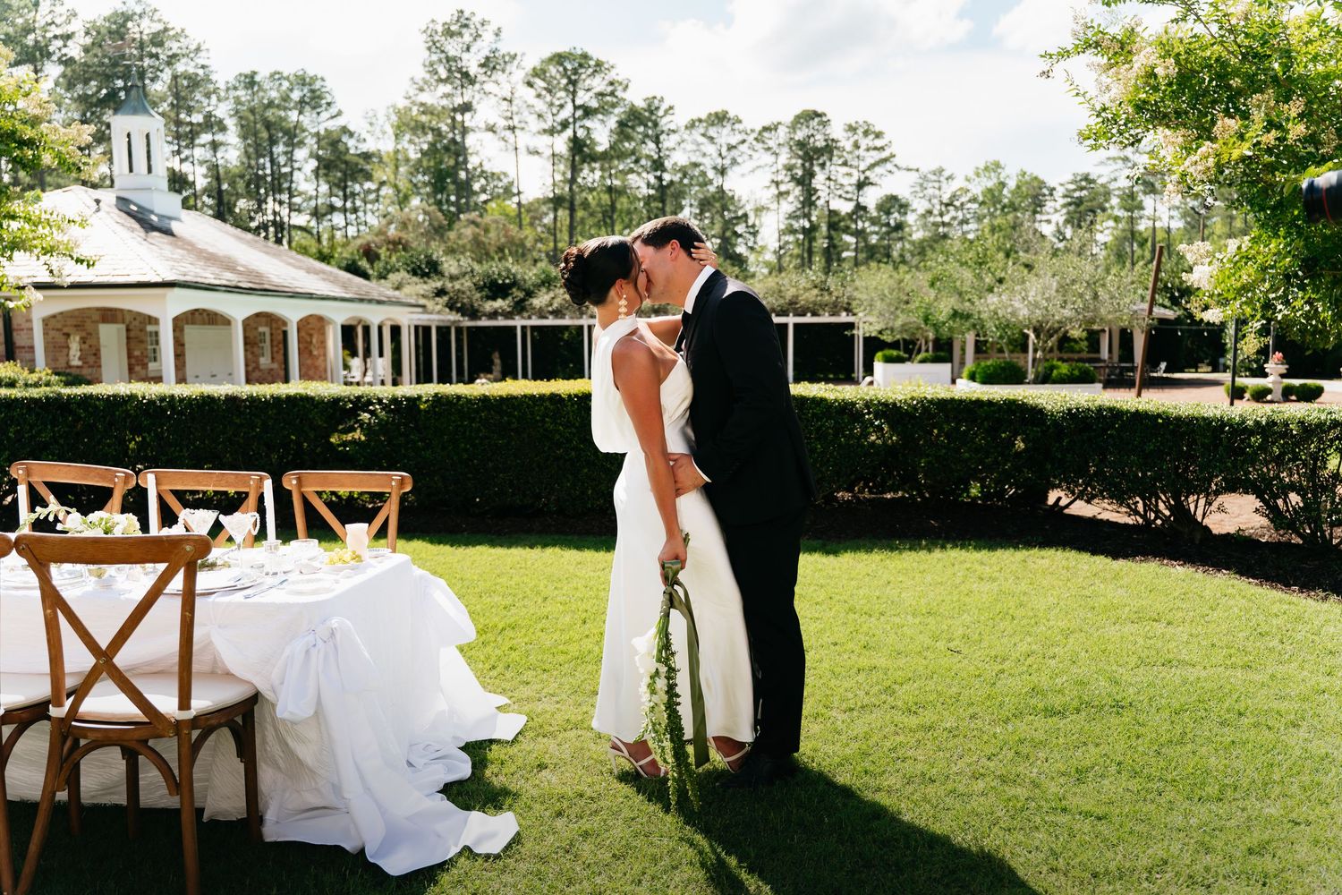 A romantic moment between a couple on their wedding day at an elegant outdoor venue with a white gazebo and manicured lawn.