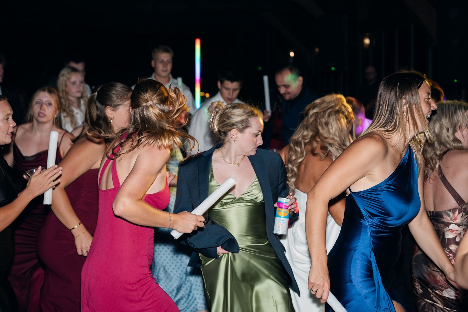 Guests in colorful formal dresses dancing at a lively wedding reception party at night.