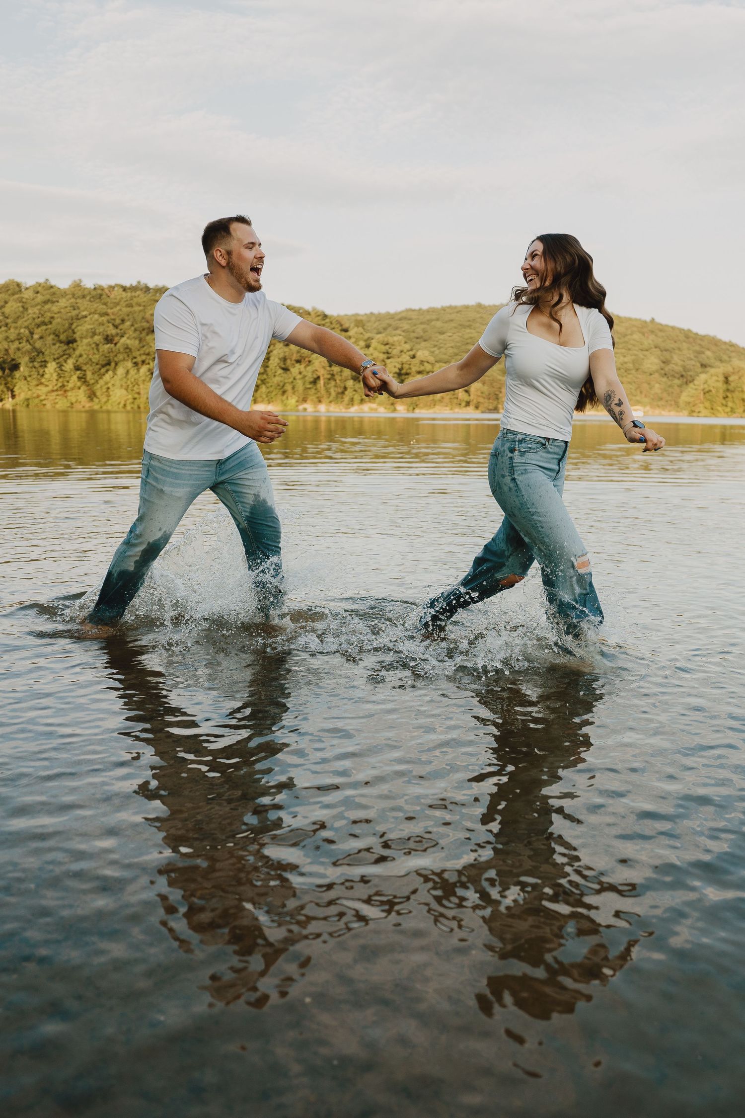 A couple holds hands while splashing through the lake water at sunset.