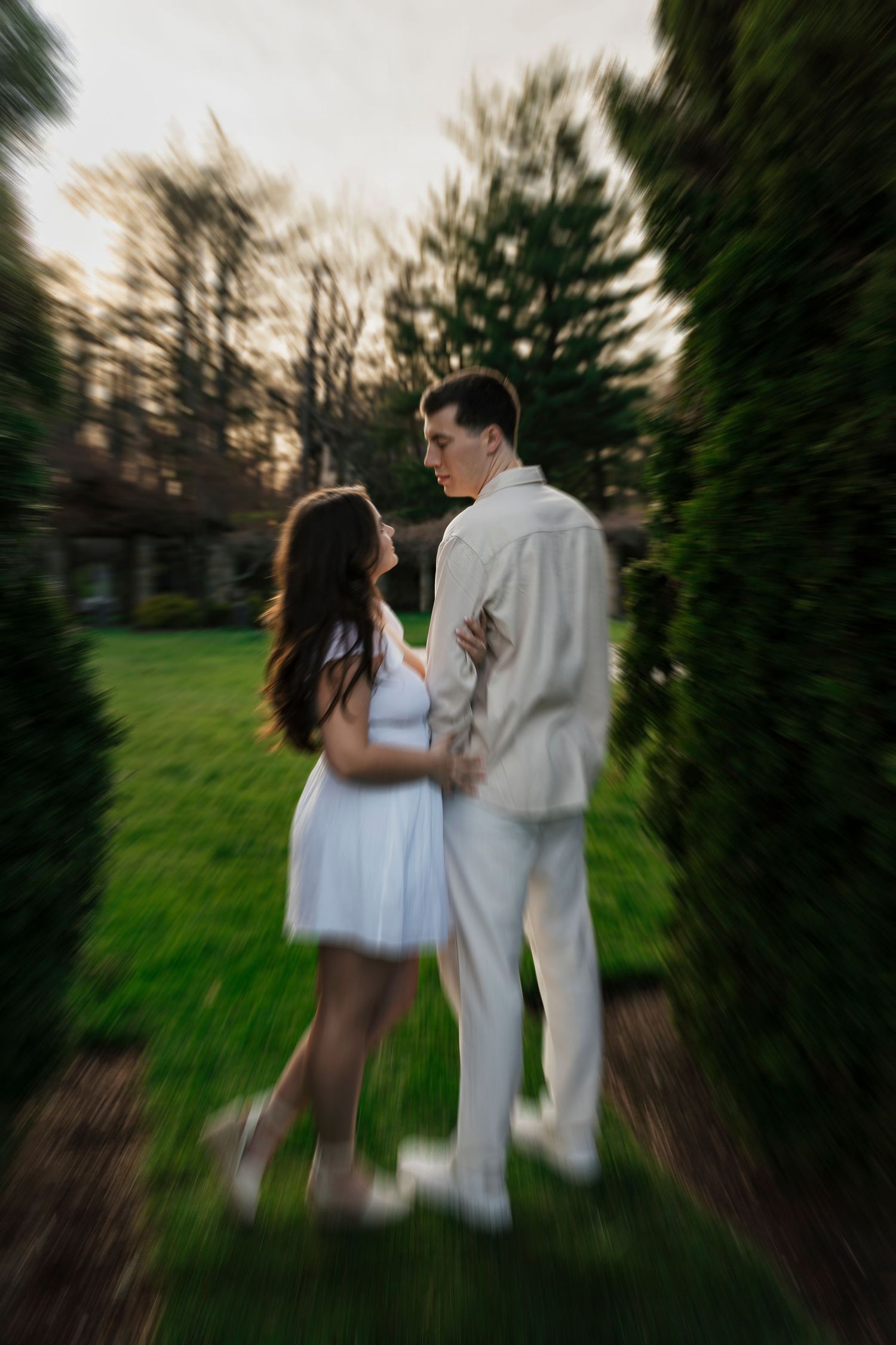 Elegant engagement portrait of couple in white outfits against 106-year-old estate garden in Loretto PA