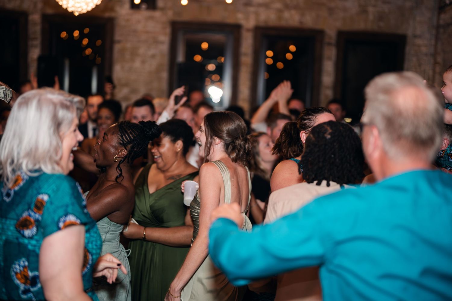 Guests dancing joyfully at a wedding reception in an elegant venue with warm string lights.