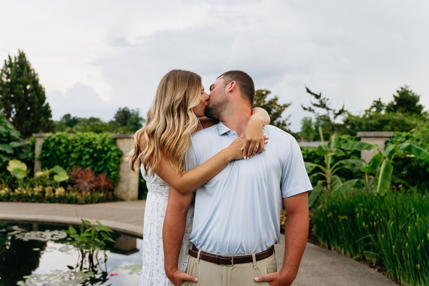 Couple sharing romantic kisses in a lush garden setting during a summer wedding photo session.