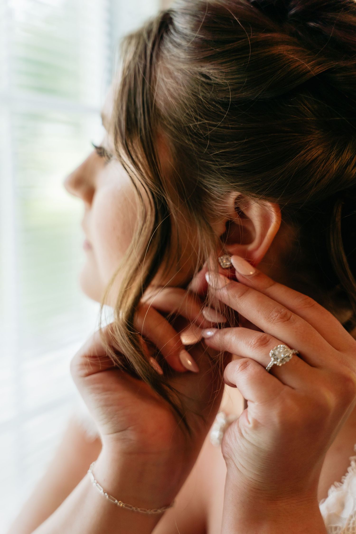 Close-up side view showing hands putting on an elegant diamond engagement ring and delicate bracelet.