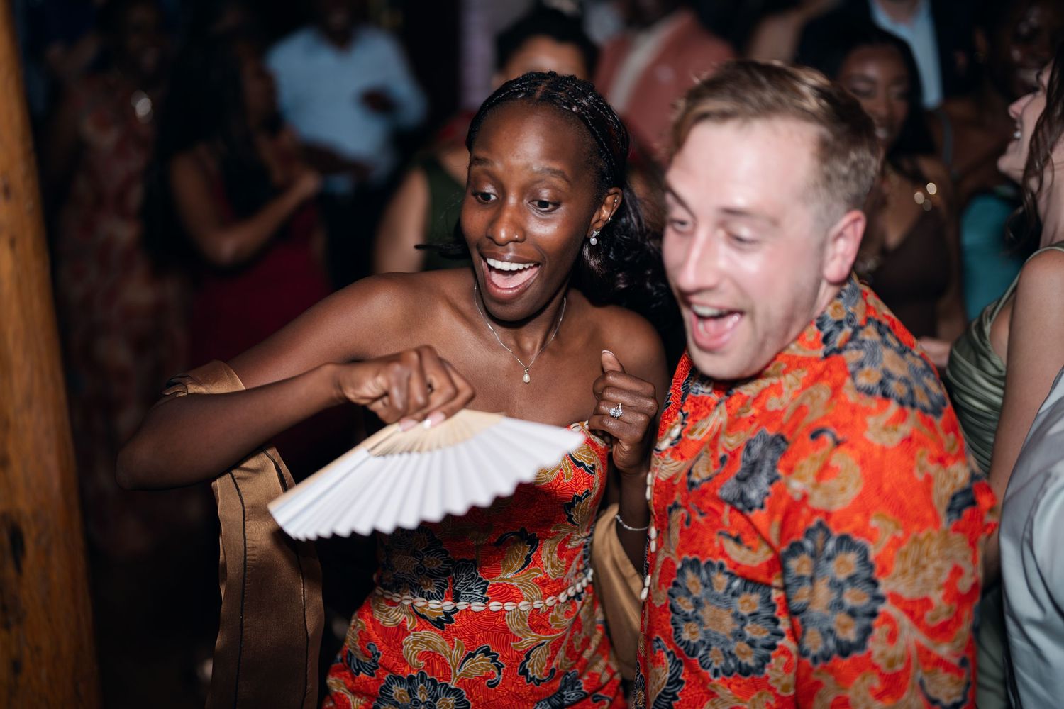 Couple laughing and dancing joyfully at wedding reception in vibrant floral attire.