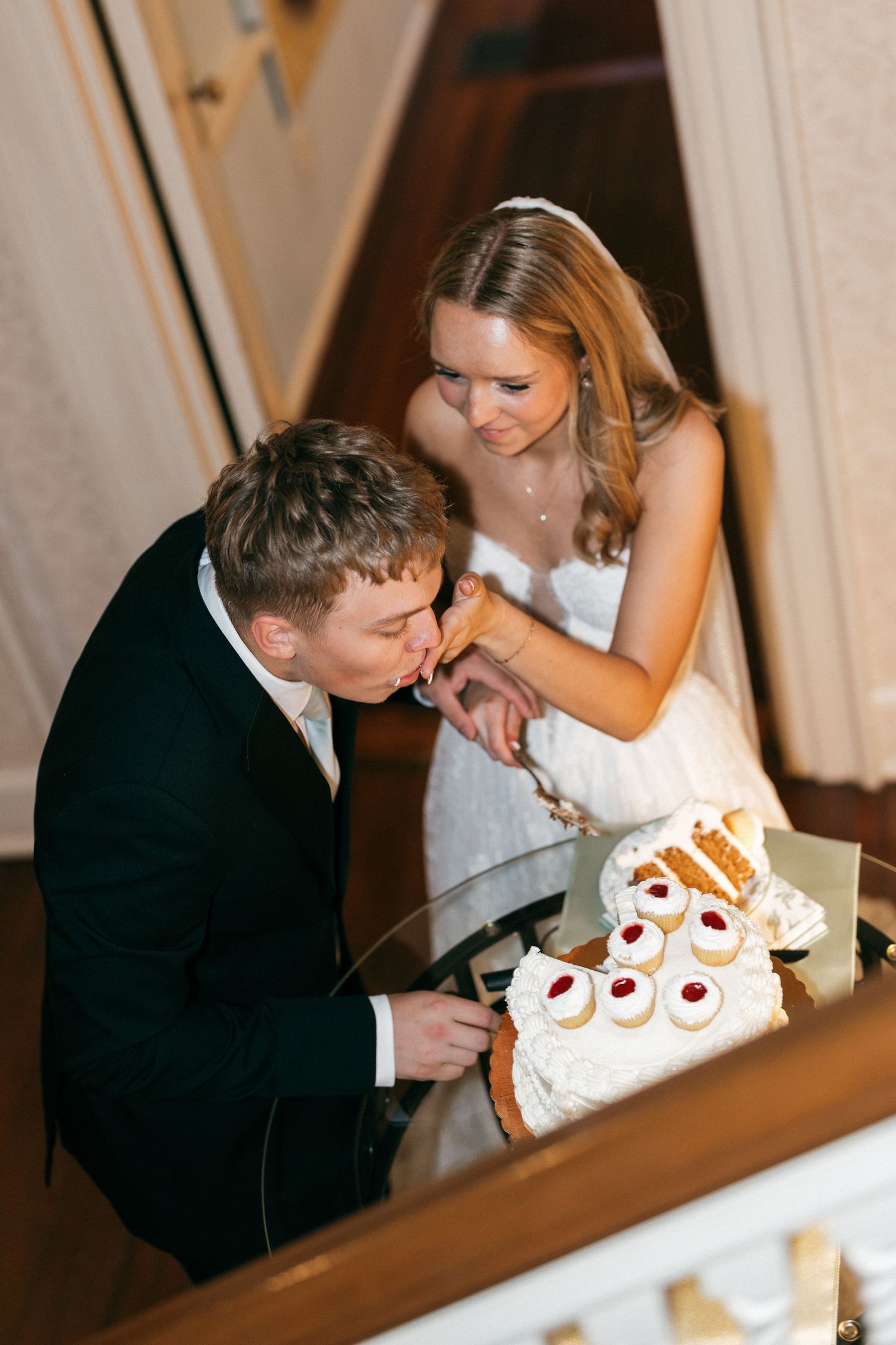 Bride and groom cutting their wedding cake together, smiling joyfully at an elegant indoor reception.