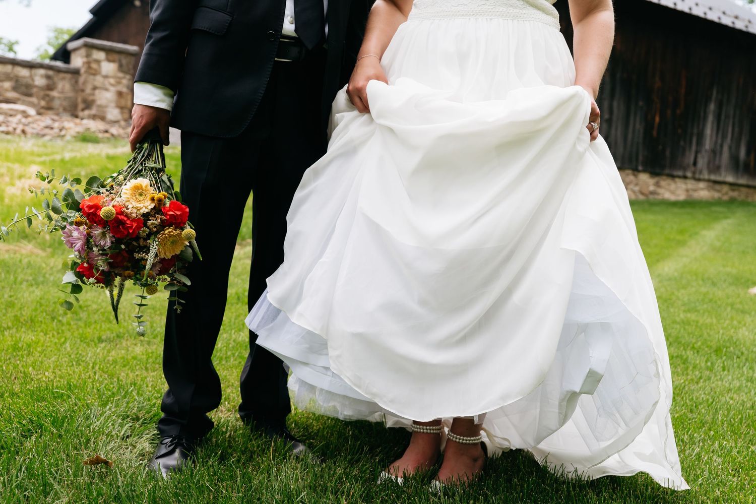 Wedding party members helping to lift and carry a white wedding dress train across a grassy outdoor venue.