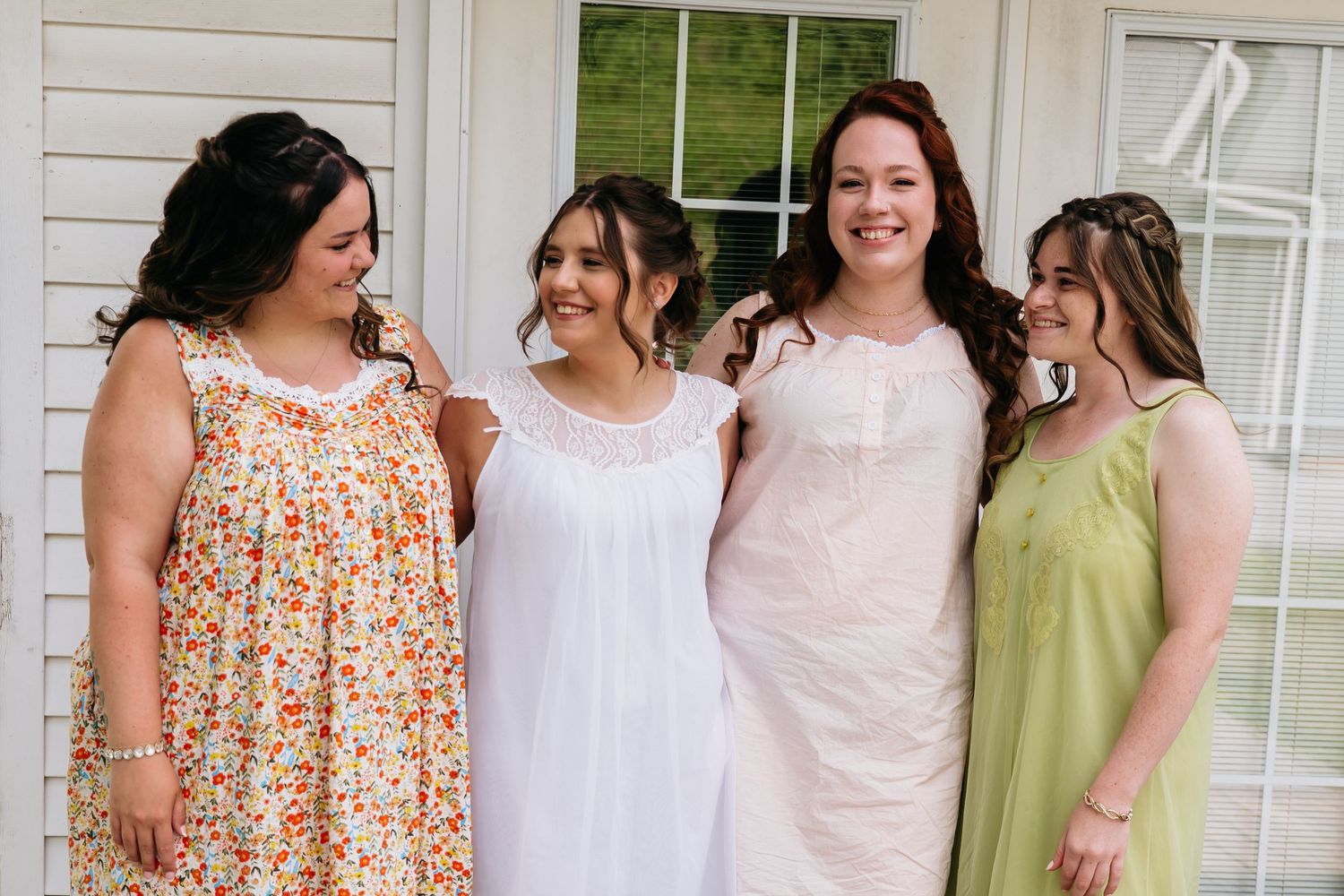 Four friends share a joyful moment while wearing summer dresses in floral, white, pink and sage green colors.