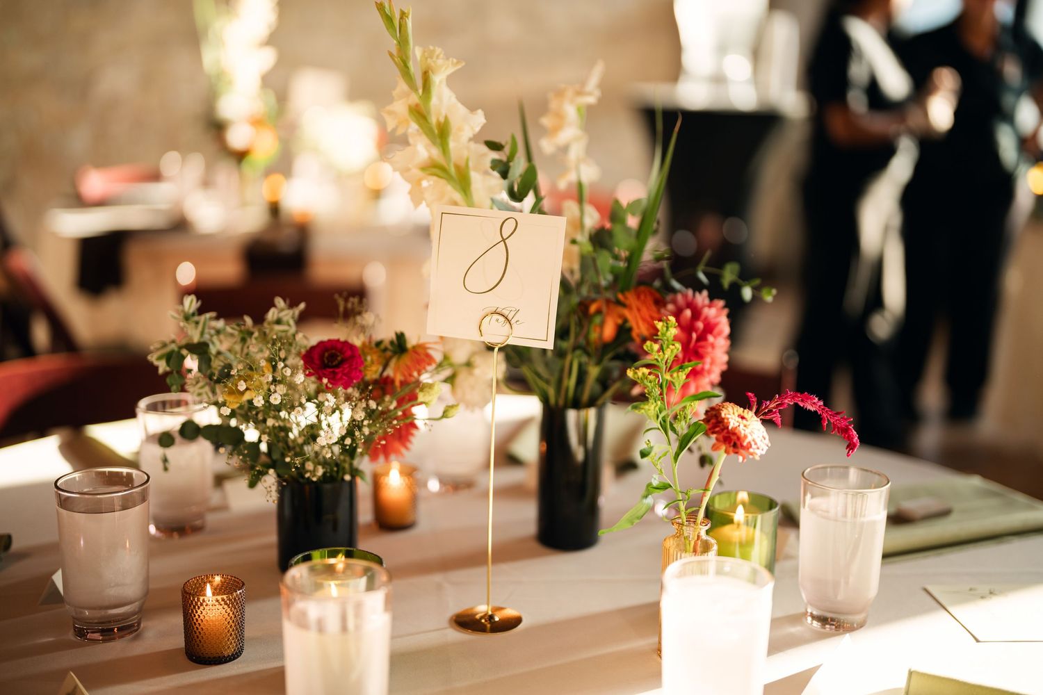 Elegant wedding reception table with colorful floral arrangements, candles, and a table number card centerpiece.