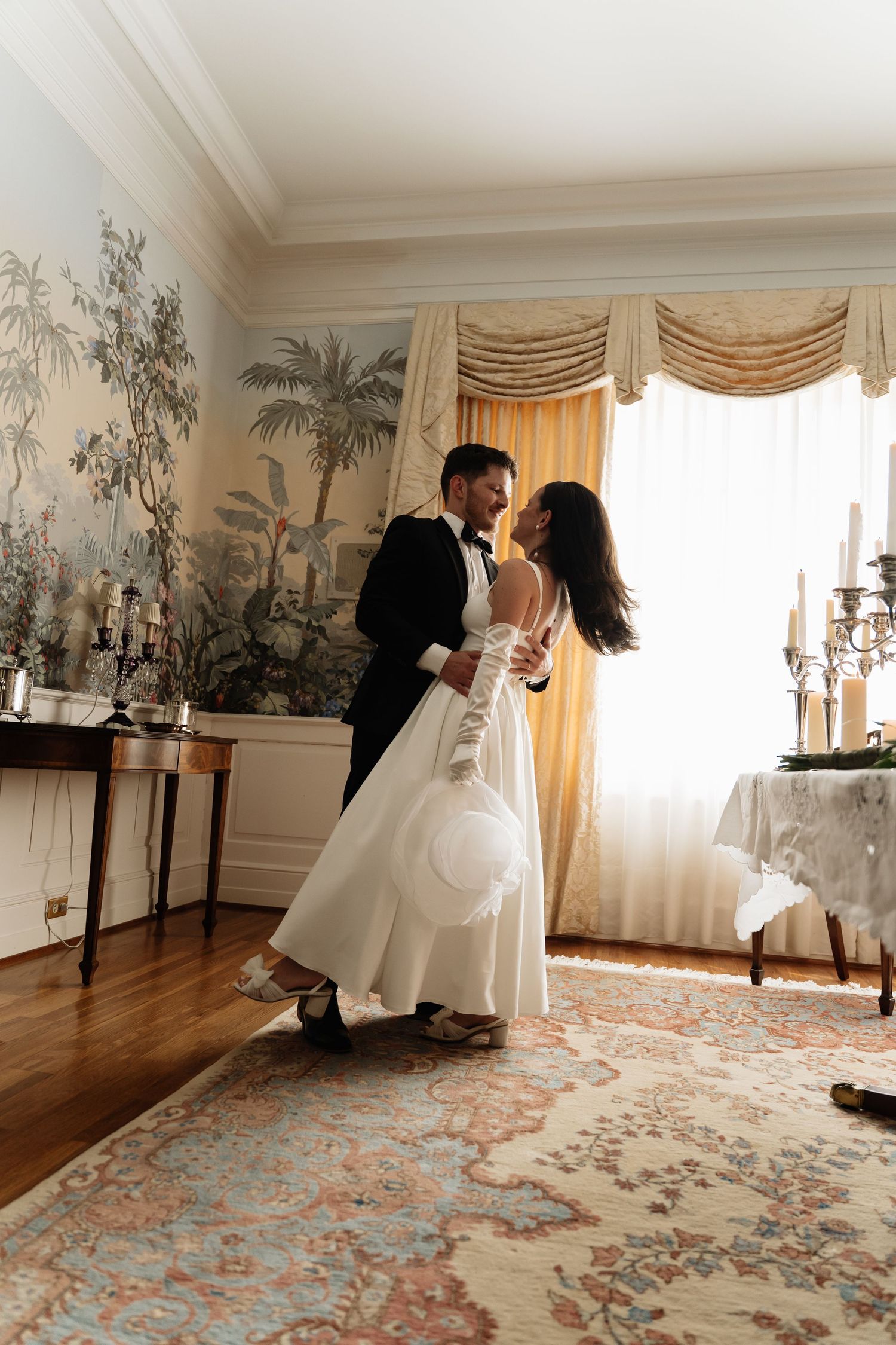 A romantic dance sequence captured in an elegant room with floral wallpaper and a patterned carpet.