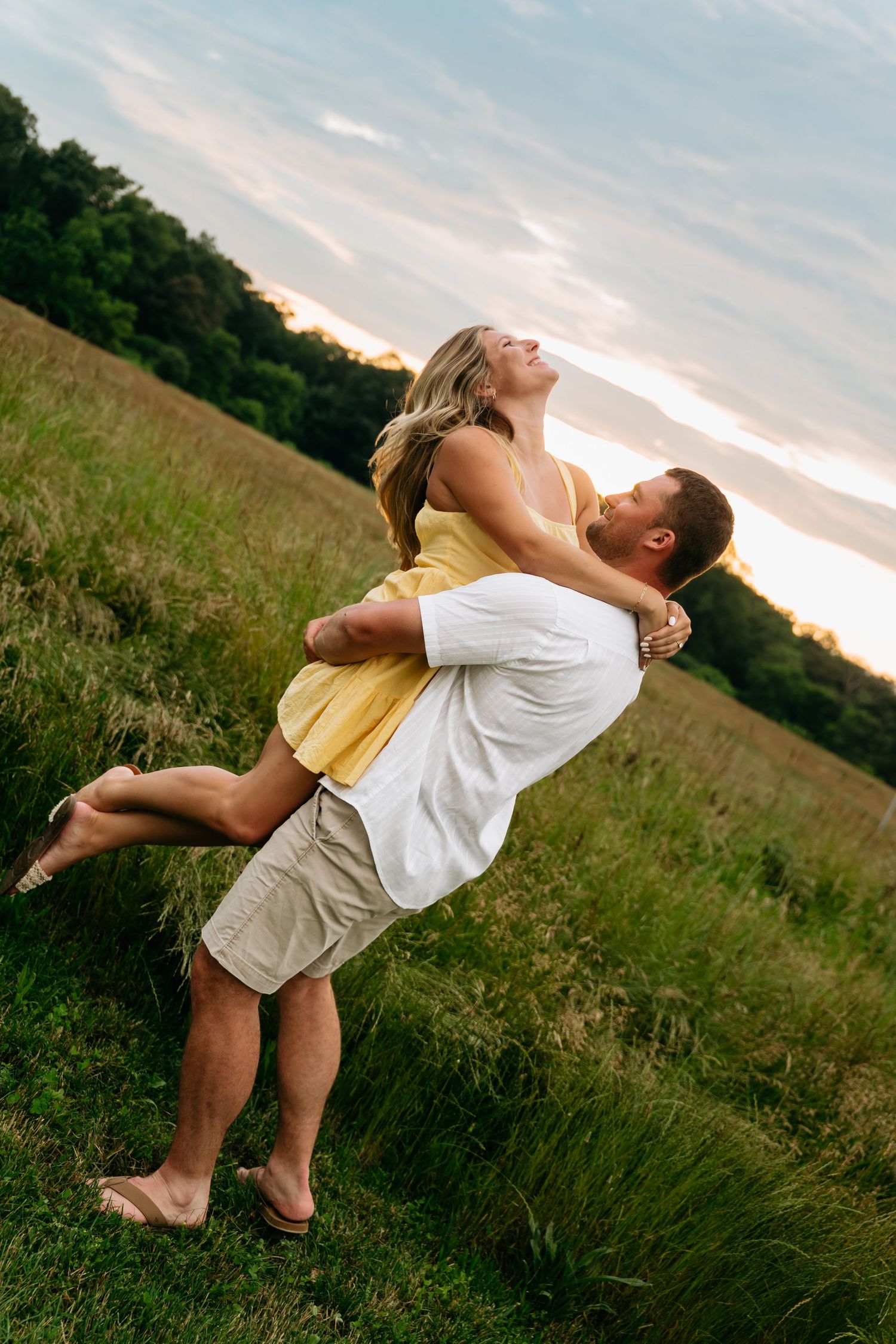 A couple in a grassy field performs a romantic dance dip pose at sunset.