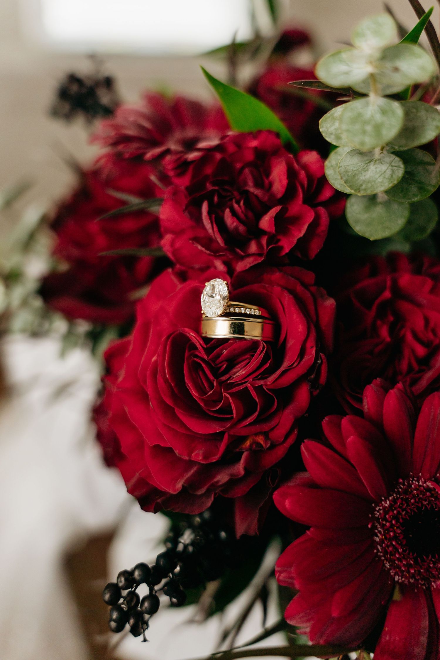 Deep red roses with diamond engagement rings nestled among the petals create an elegant wedding photography detail shot.