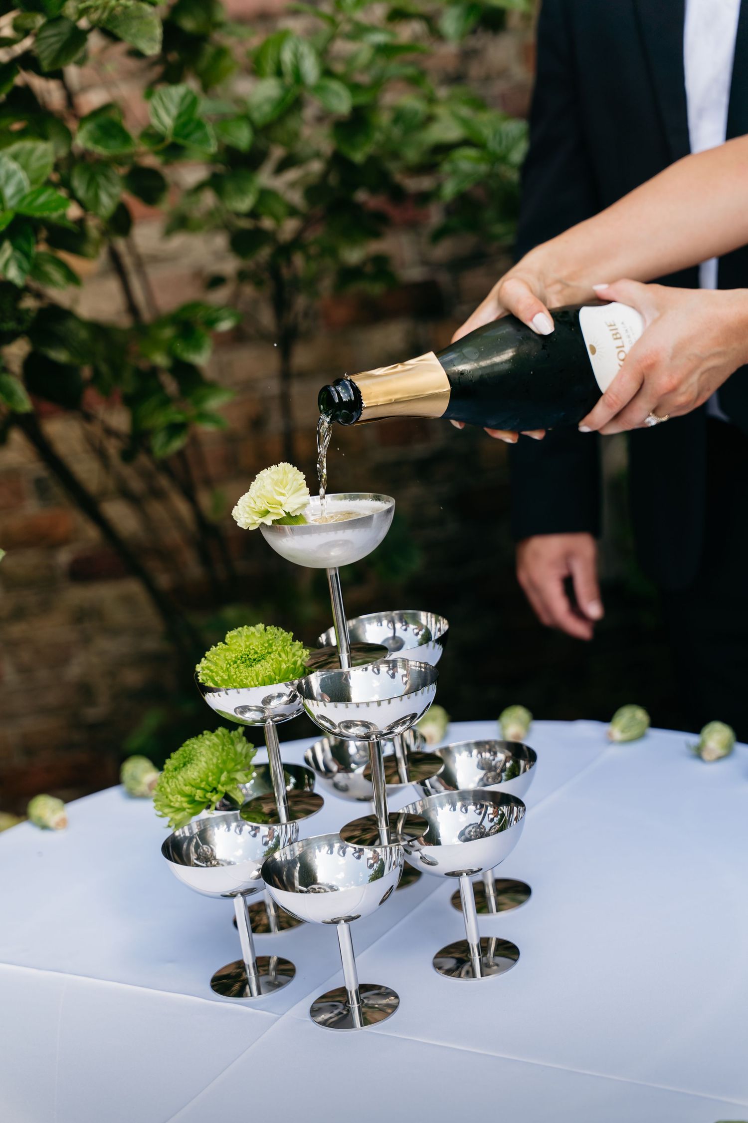 Champagne being poured into elegant silver tiered serving dishes on a white tablecloth at an upscale event.