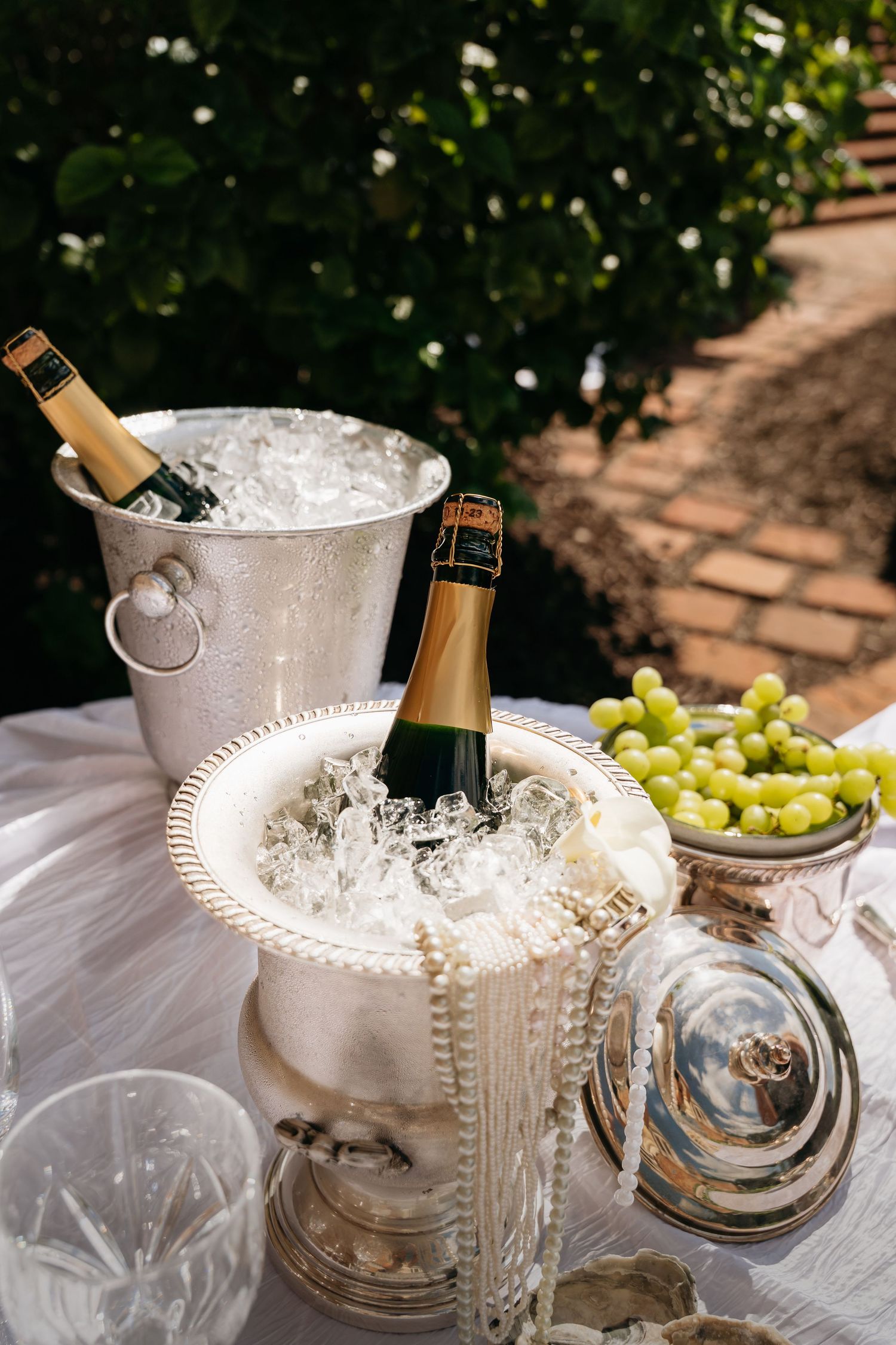 Champagne bottles chilling in ice buckets with fresh green grapes on an elegant table setting outdoors.