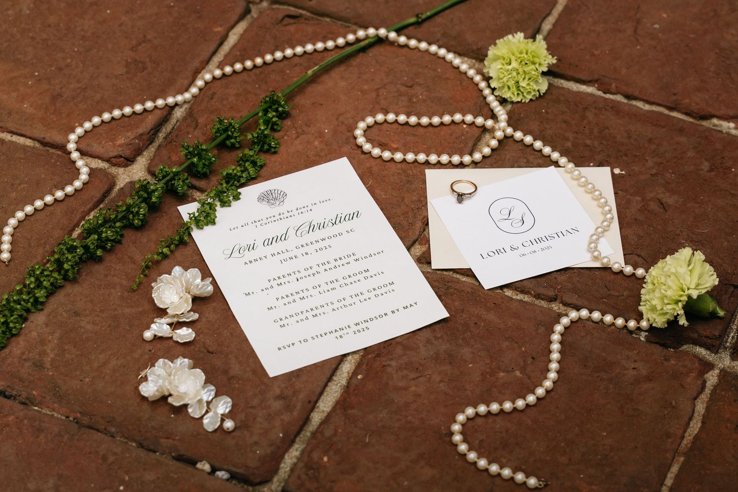 Pearl necklace and wedding stationery arranged on rustic wooden surface with delicate white flowers and greenery.