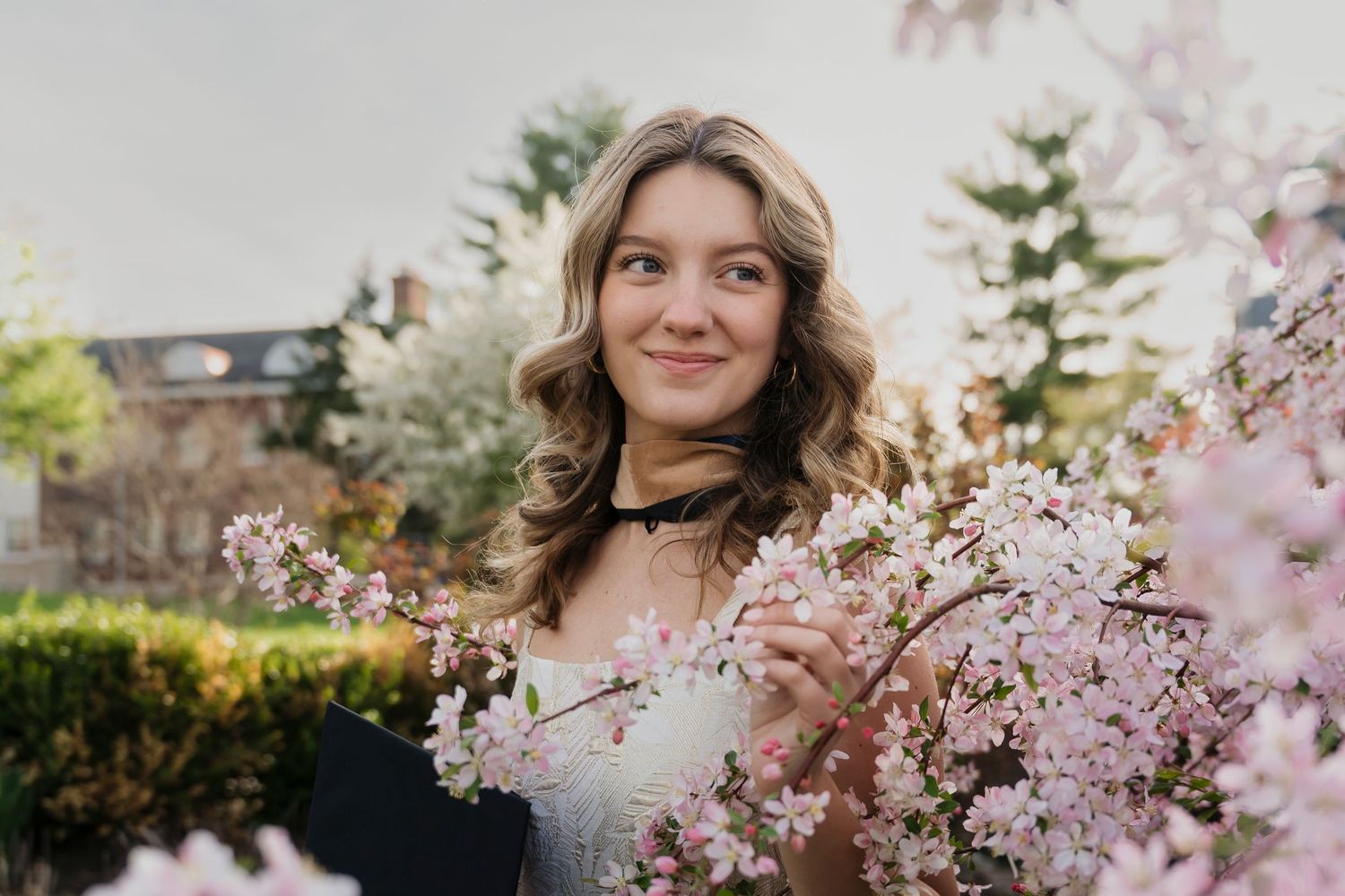 A springtime grad portrait surrounded by delicate pink cherry blossoms in a garden setting.
