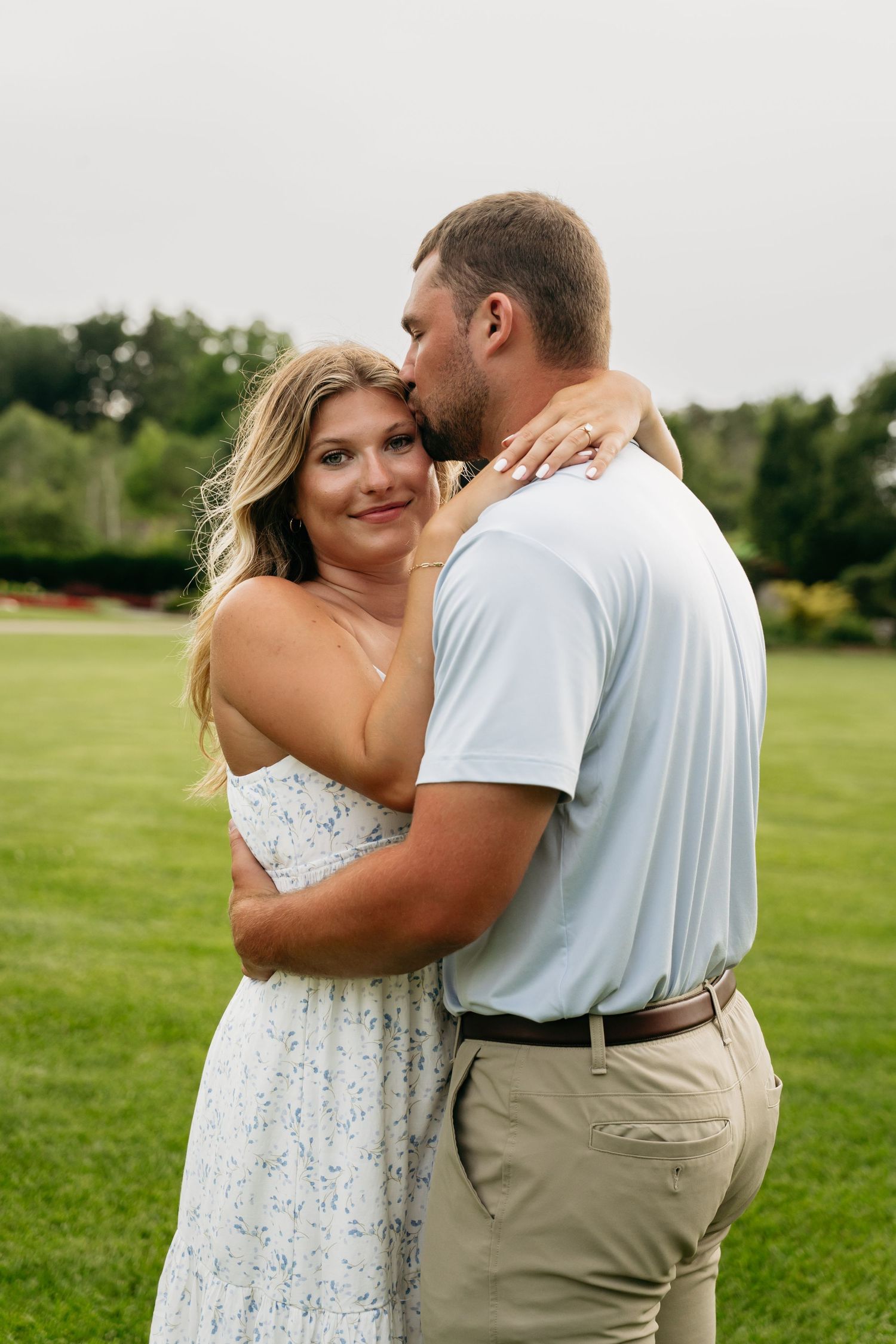 A romantic couple embraces in a grassy field wearing white and khaki casual attire.