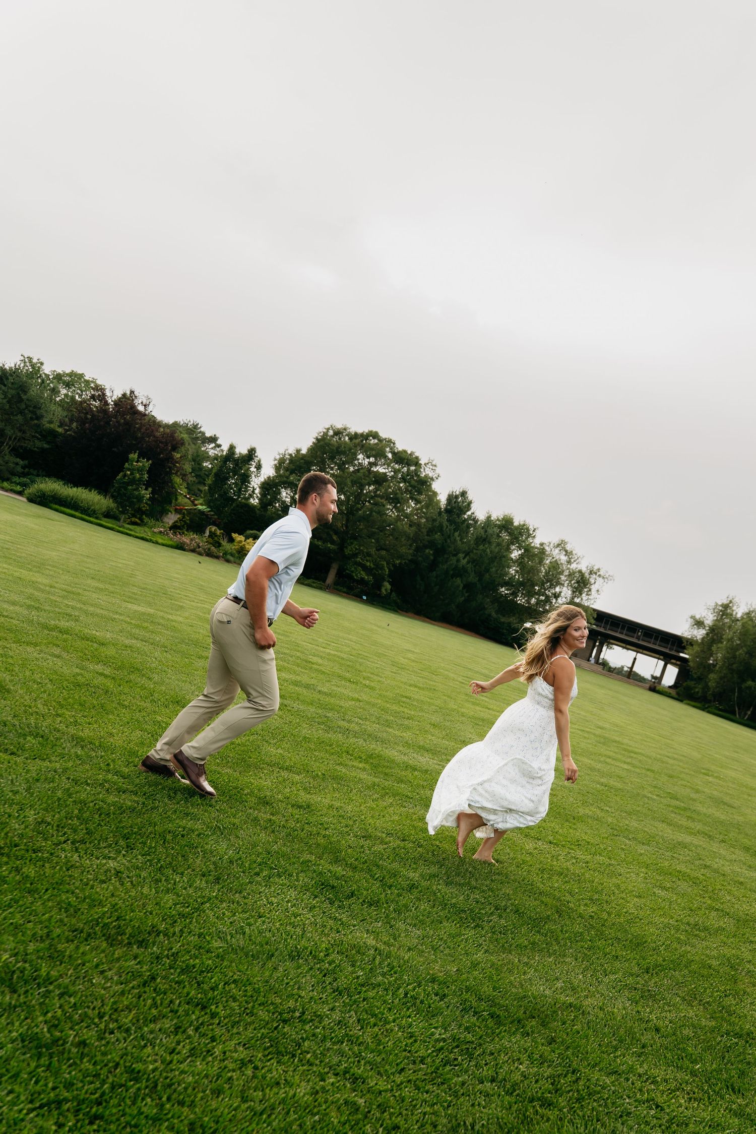 A couple playfully jumps and runs together on a green grassy hill during an outdoor photo session.