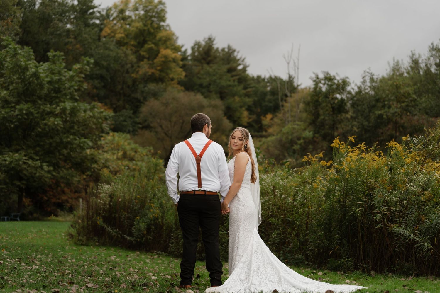 A wedding couple walks together through an outdoor setting with trees and greenery.
