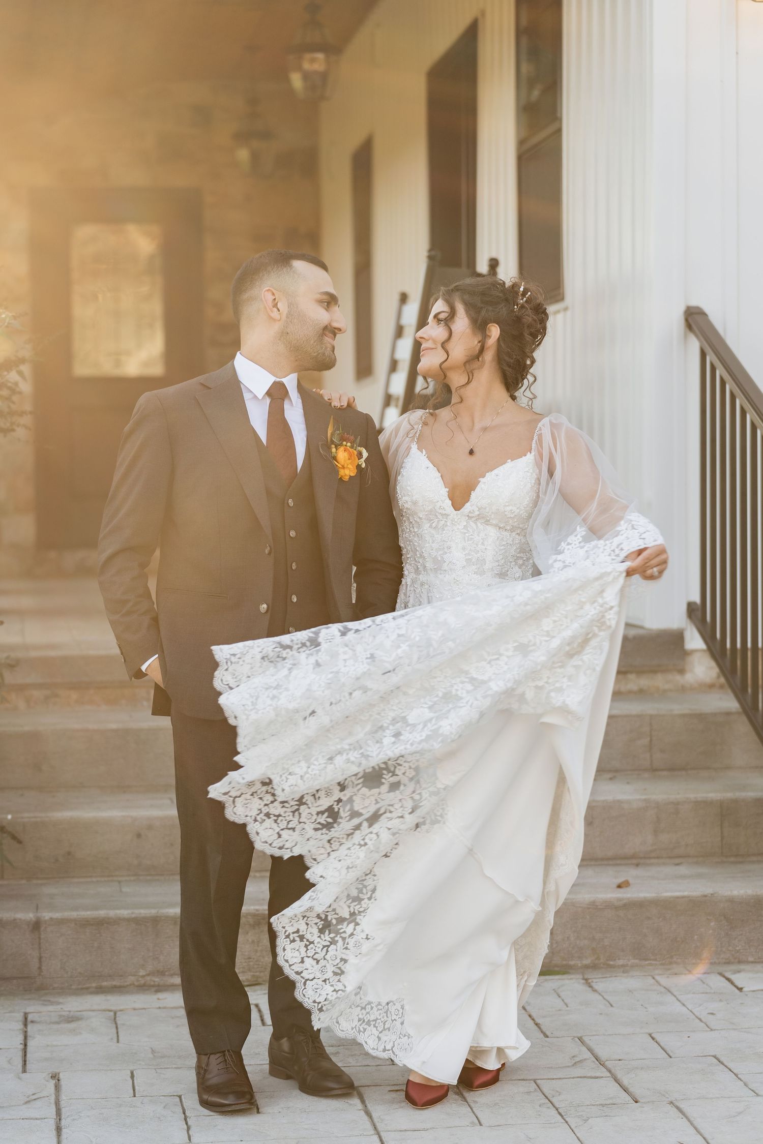 Bride shows off intricate lace details of wedding dress near classical columns.