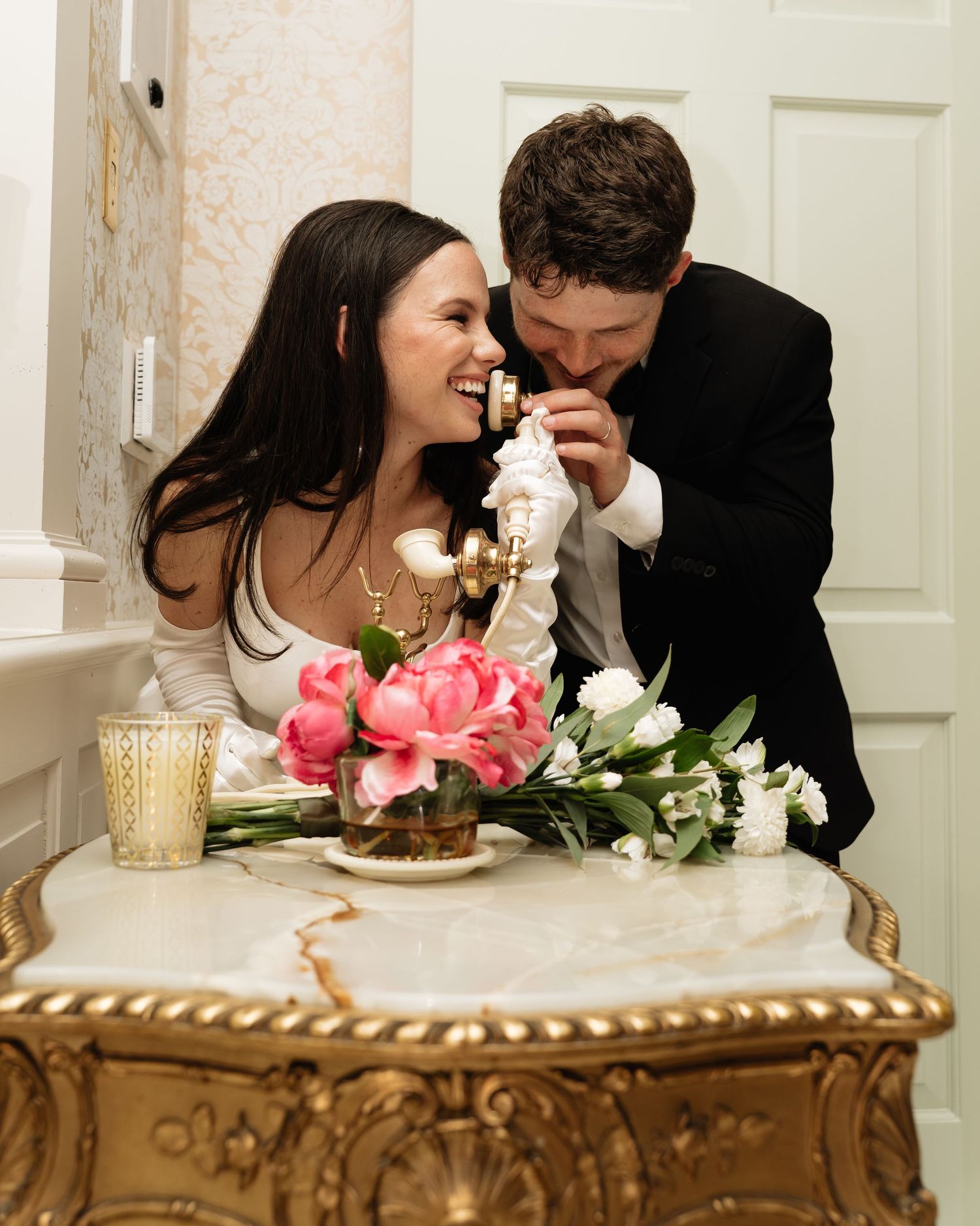 A couple shares an intimate moment at a wedding reception table decorated with pink flowers and dessert.