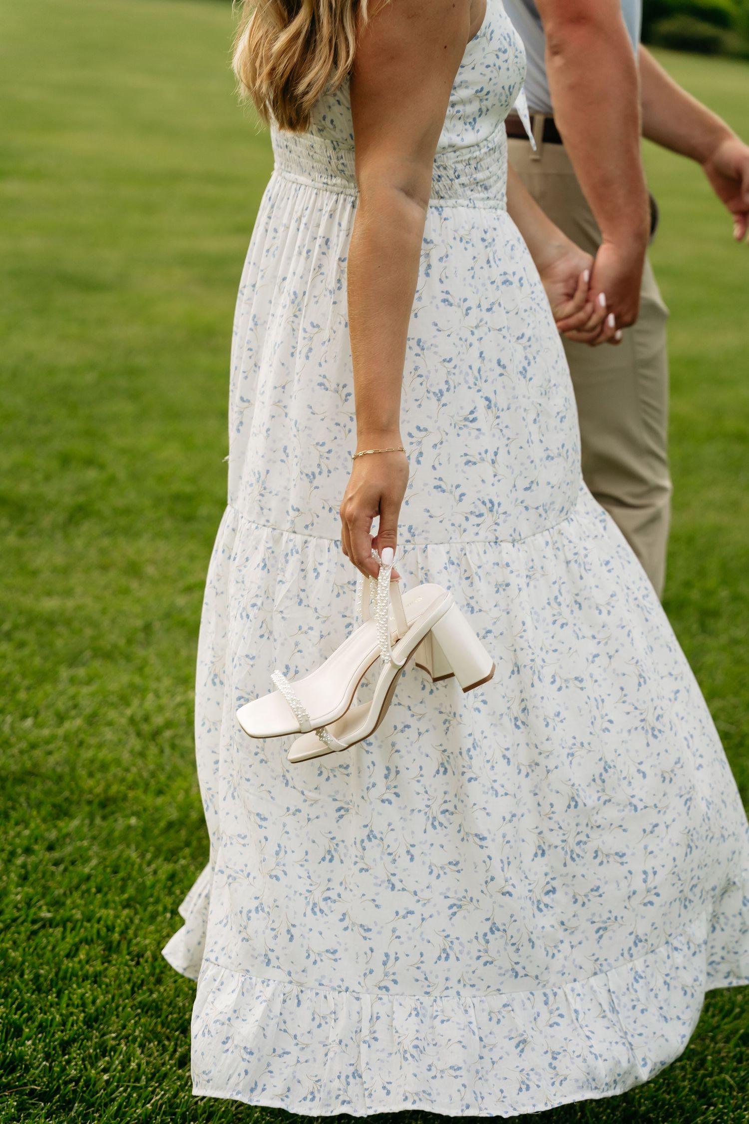 A white floral sundress with blue details is shown in a sequence of close-up shots on a green lawn.