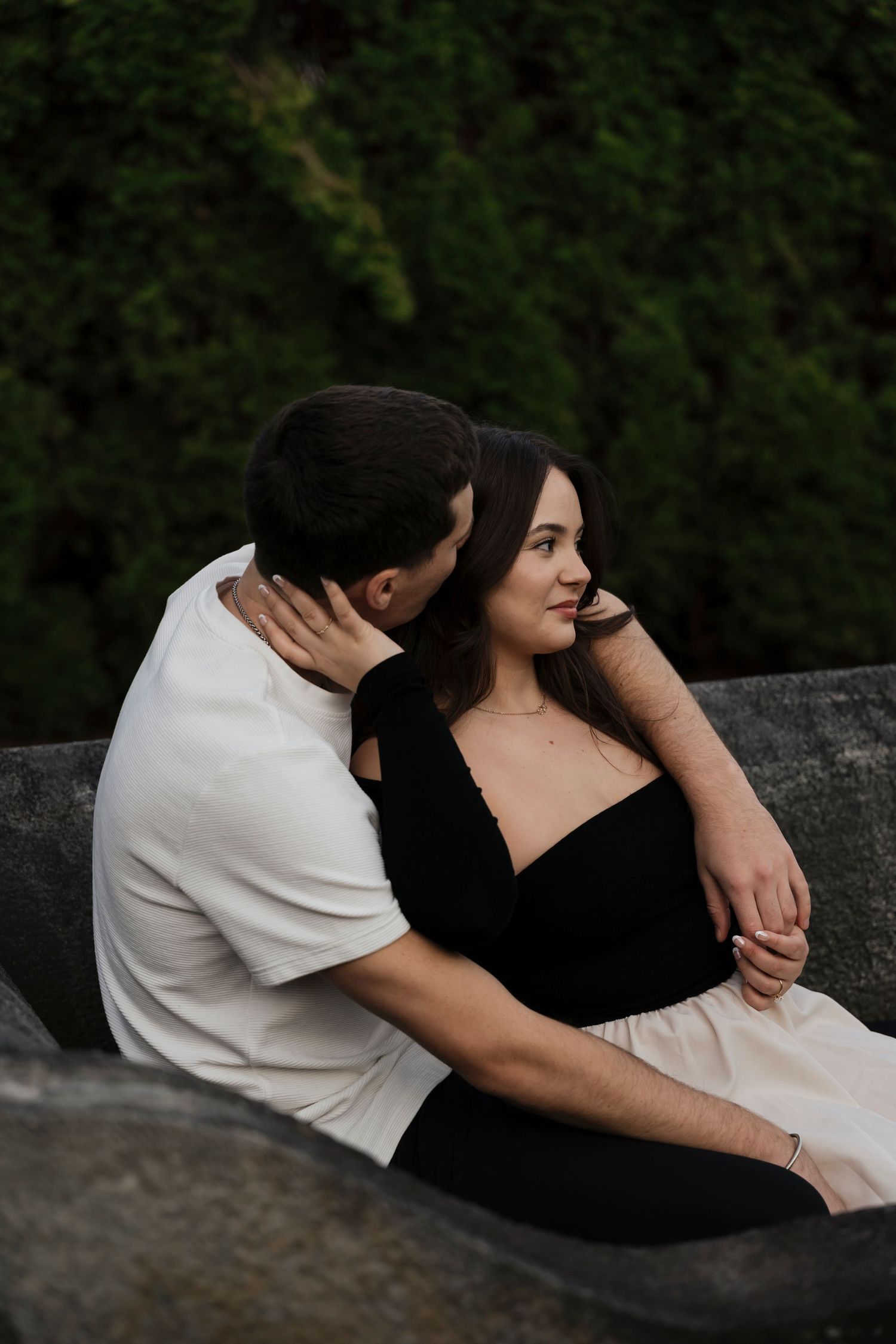 Editorial style engagement photo of couple in black attire with sunlight filtering through garden trees
