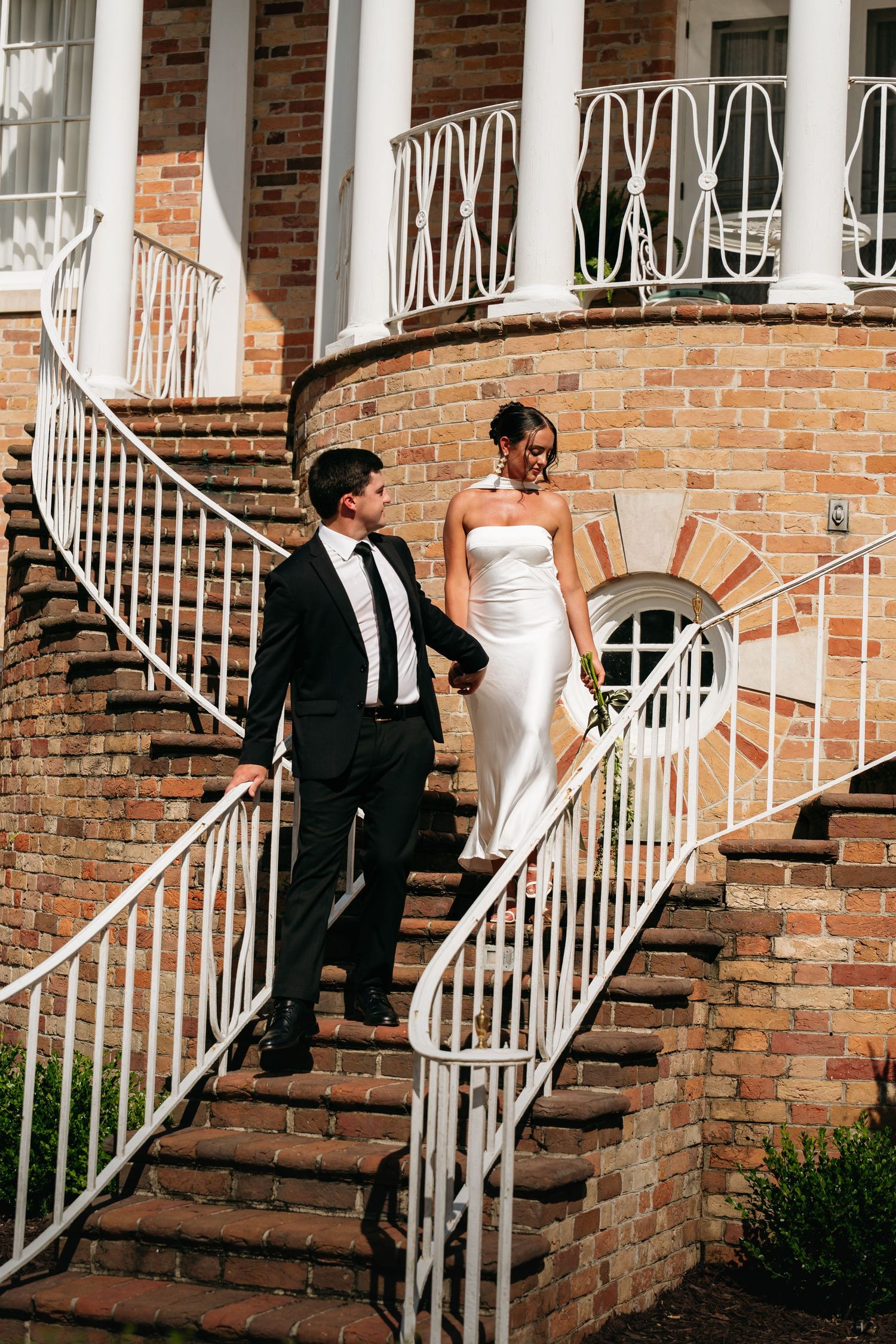 A wedding couple walks down brick steps with white railings in a sequence of four progressive photos.