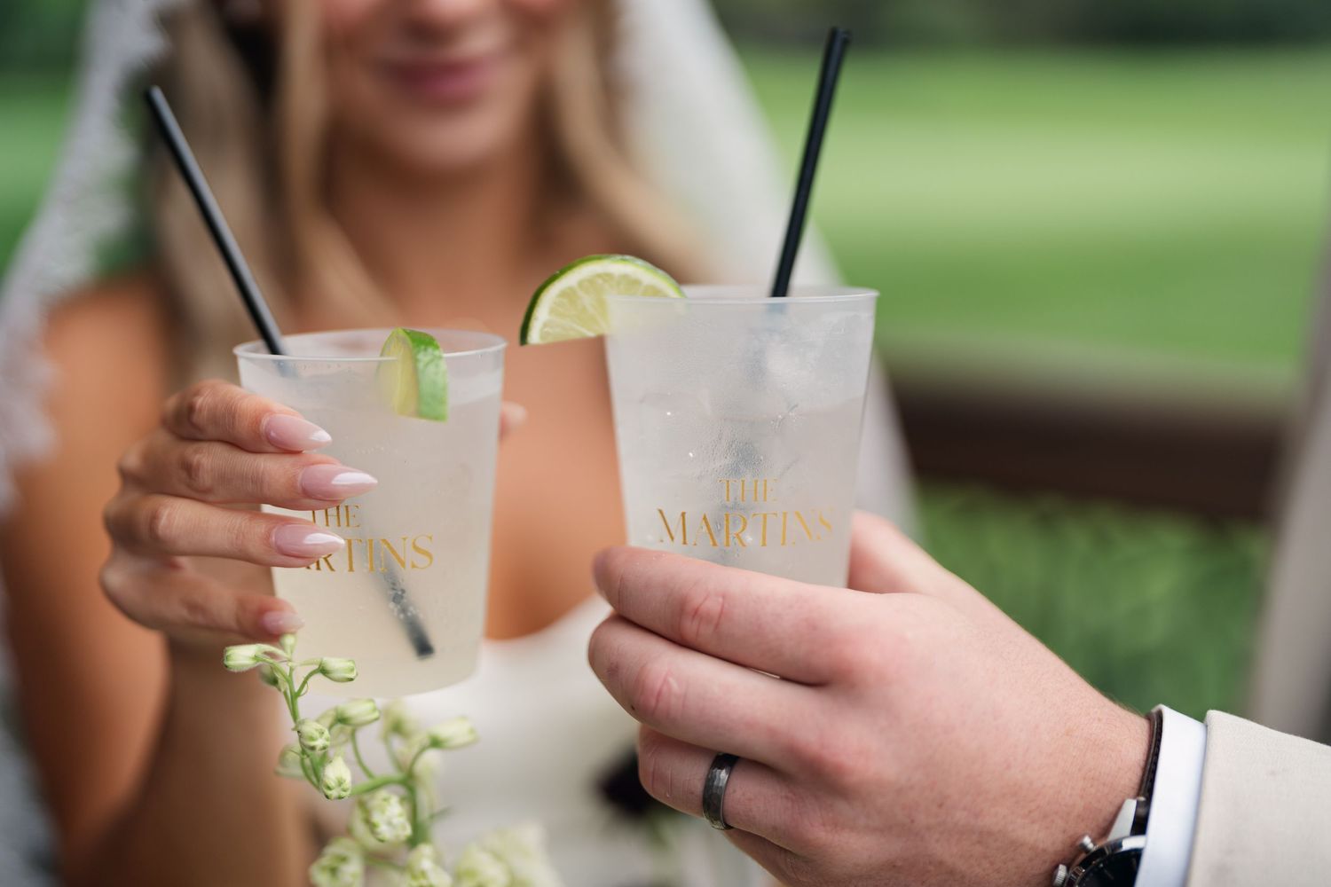 Bride and groom toasting with personalized cocktail glasses garnished with lime at an outdoor wedding reception.