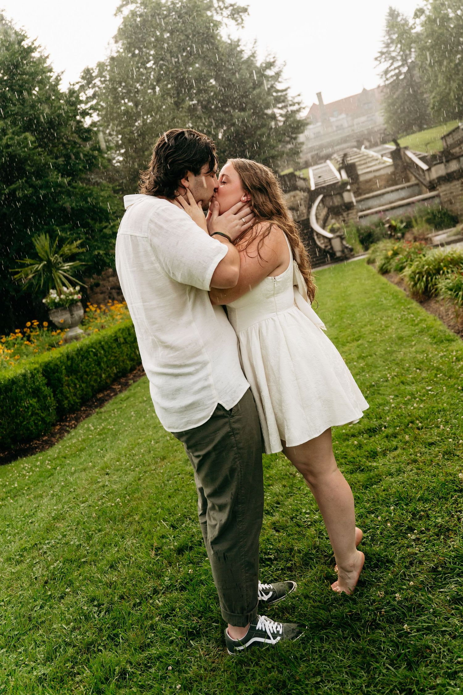 A romantic moment captured in a lush green garden setting with white and casual attire.