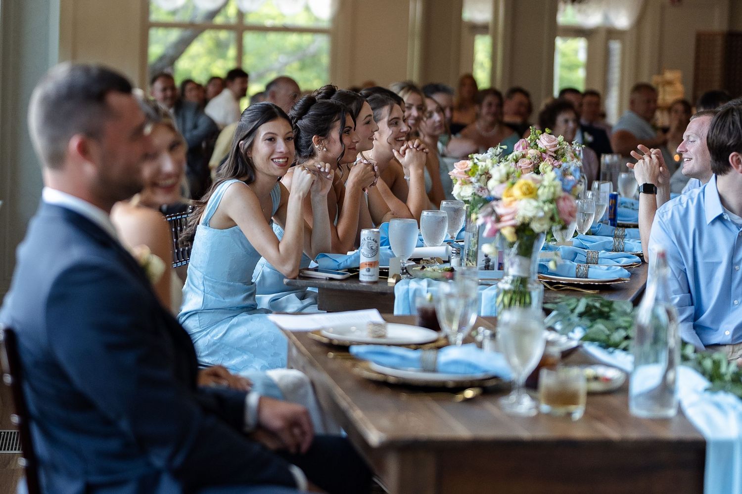 Guests laughing and smiling at a wedding reception dinner table decorated with flowers and blue linens.