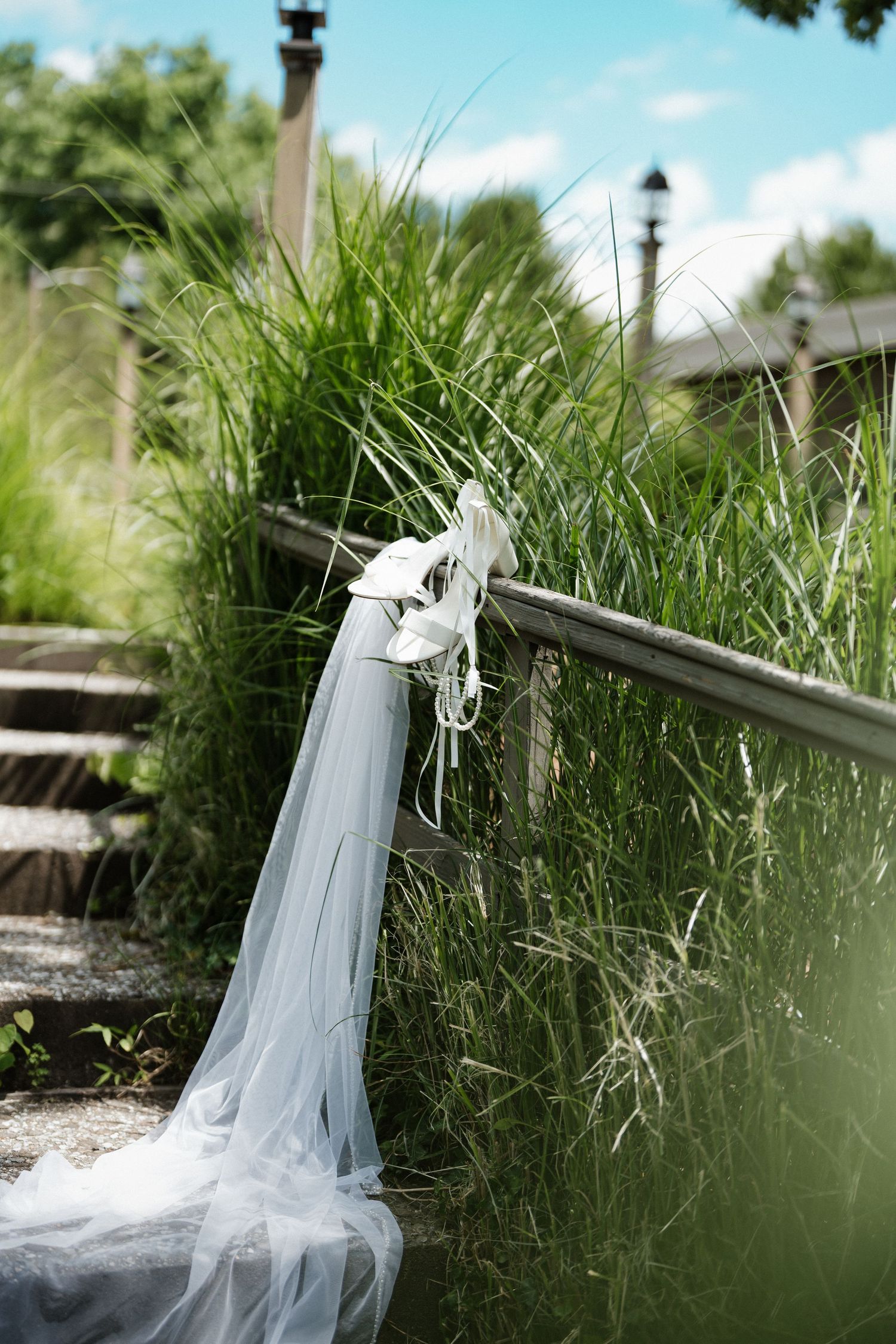 White bridal veil draped over a wooden railing surrounded by tall green grass outdoors on a sunny day.