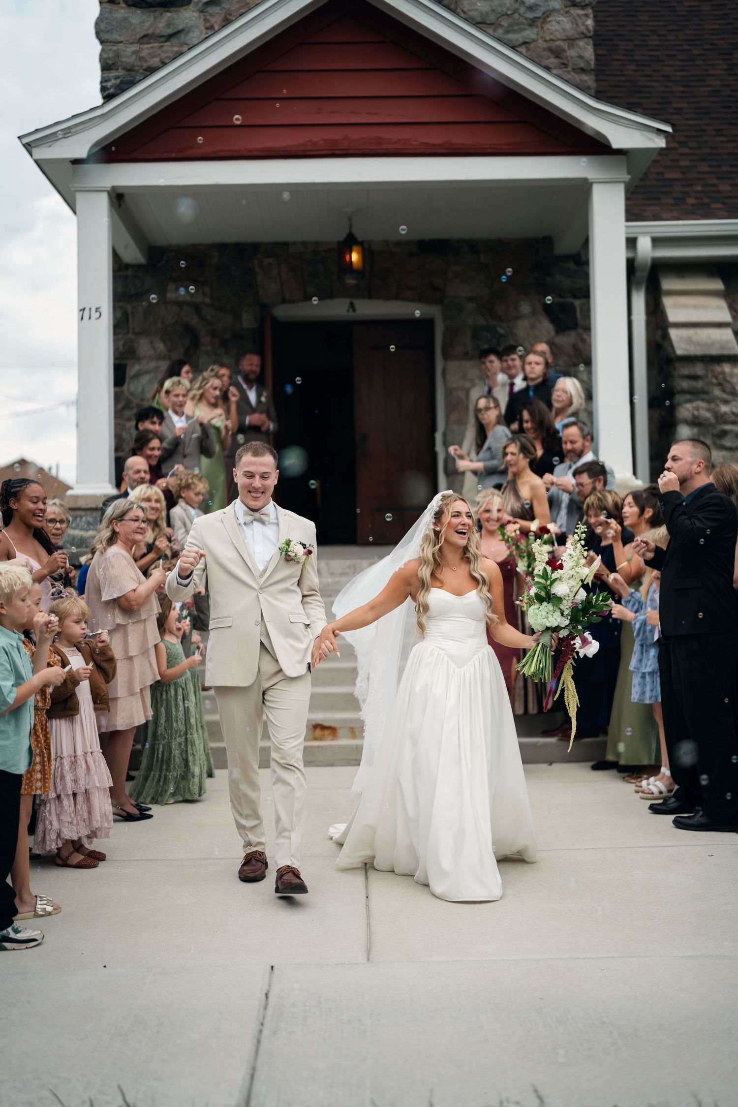 Bride and groom exit church ceremony as guests blow bubbles in joyful wedding recessional celebration.