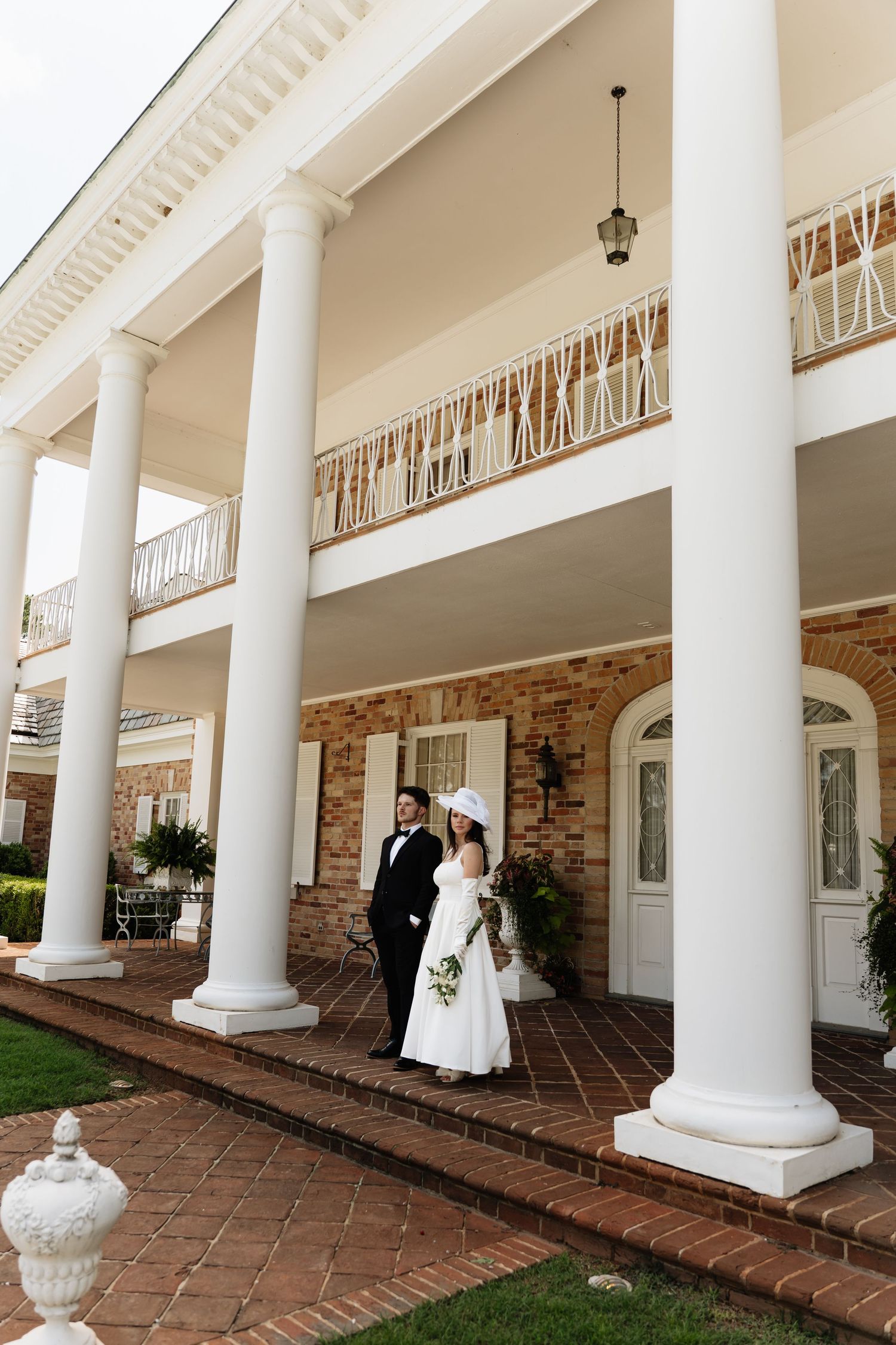 Elegant white columns line a covered brick walkway at a historic colonial-style building with ornate architectural details.