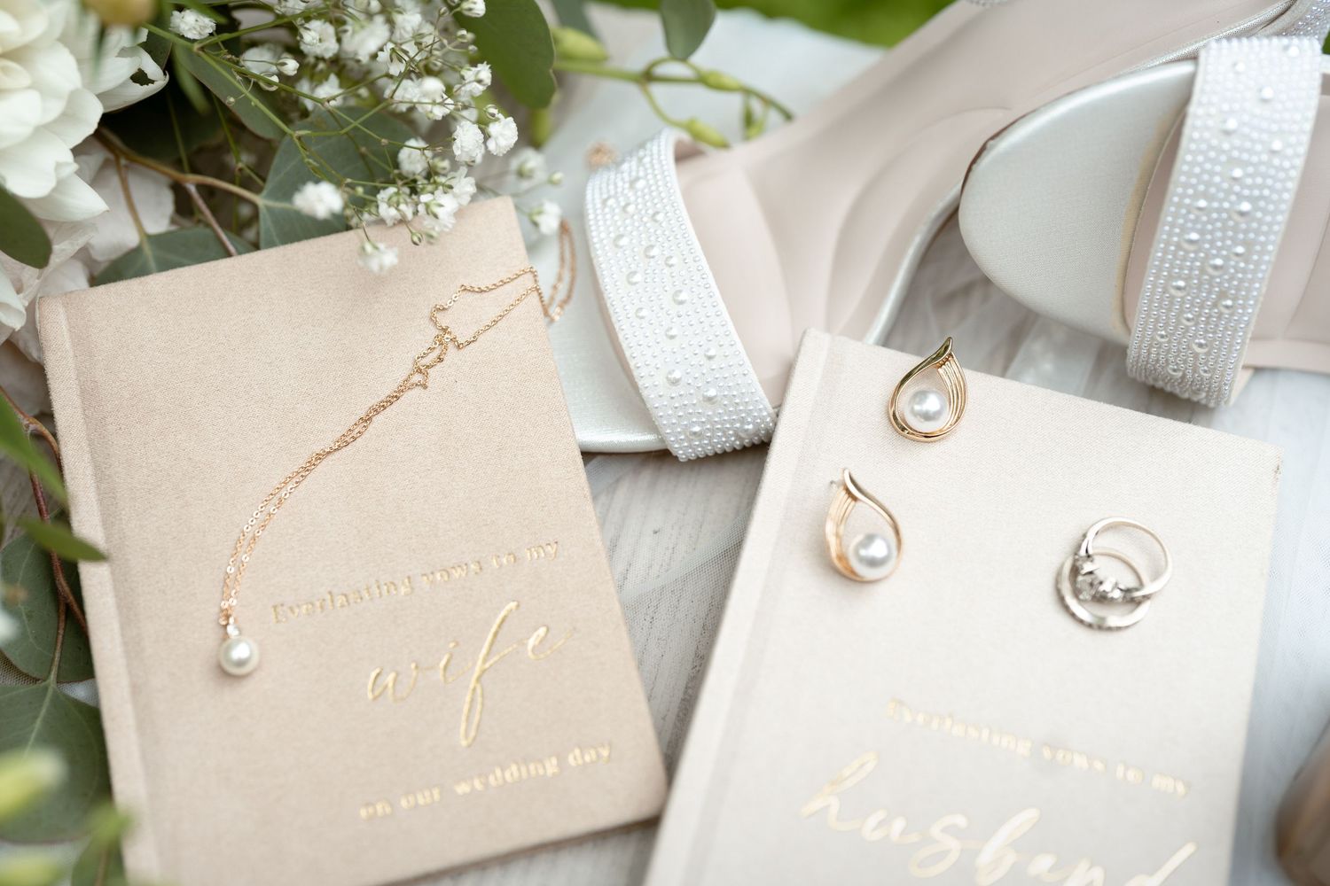 Wedding gift books for wife and husband with pearl jewelry, rose gold necklace, and white ribbon on neutral background.